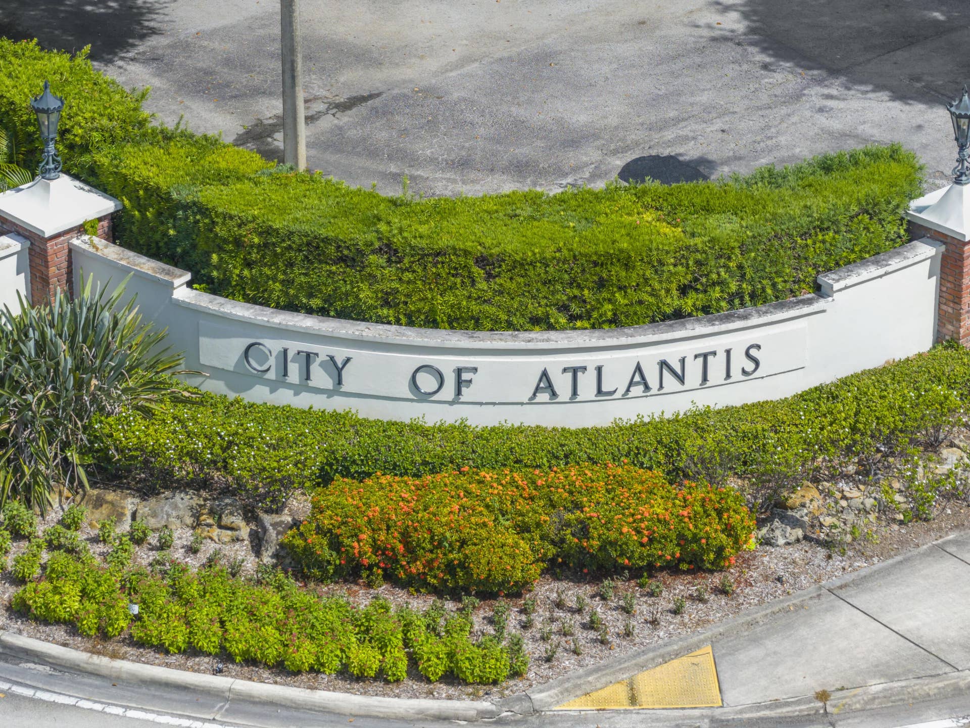 137 Clubhouse Boulevard, Atlantis, FL 33462 Curved masonry signage with brick pillar accents, integrated lighting fixtures, and professional landscaping featuring manicured hedges and ornamental shrubs