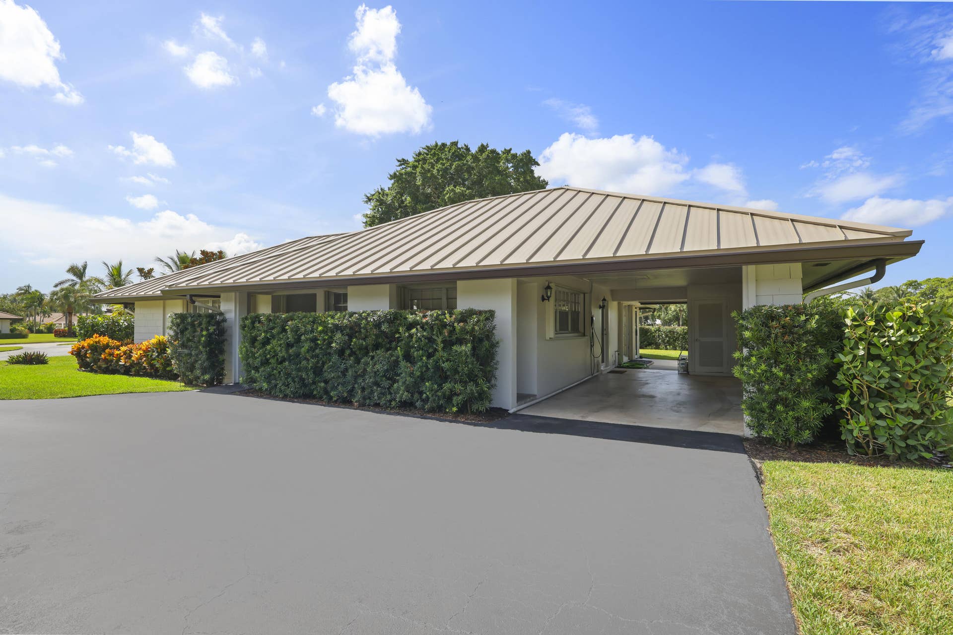 137 Clubhouse Boulevard, Atlantis, FL 33462 Single-story exterior featuring a standing-seam metal roof, integrated carport, paved driveway, and manicured landscaping