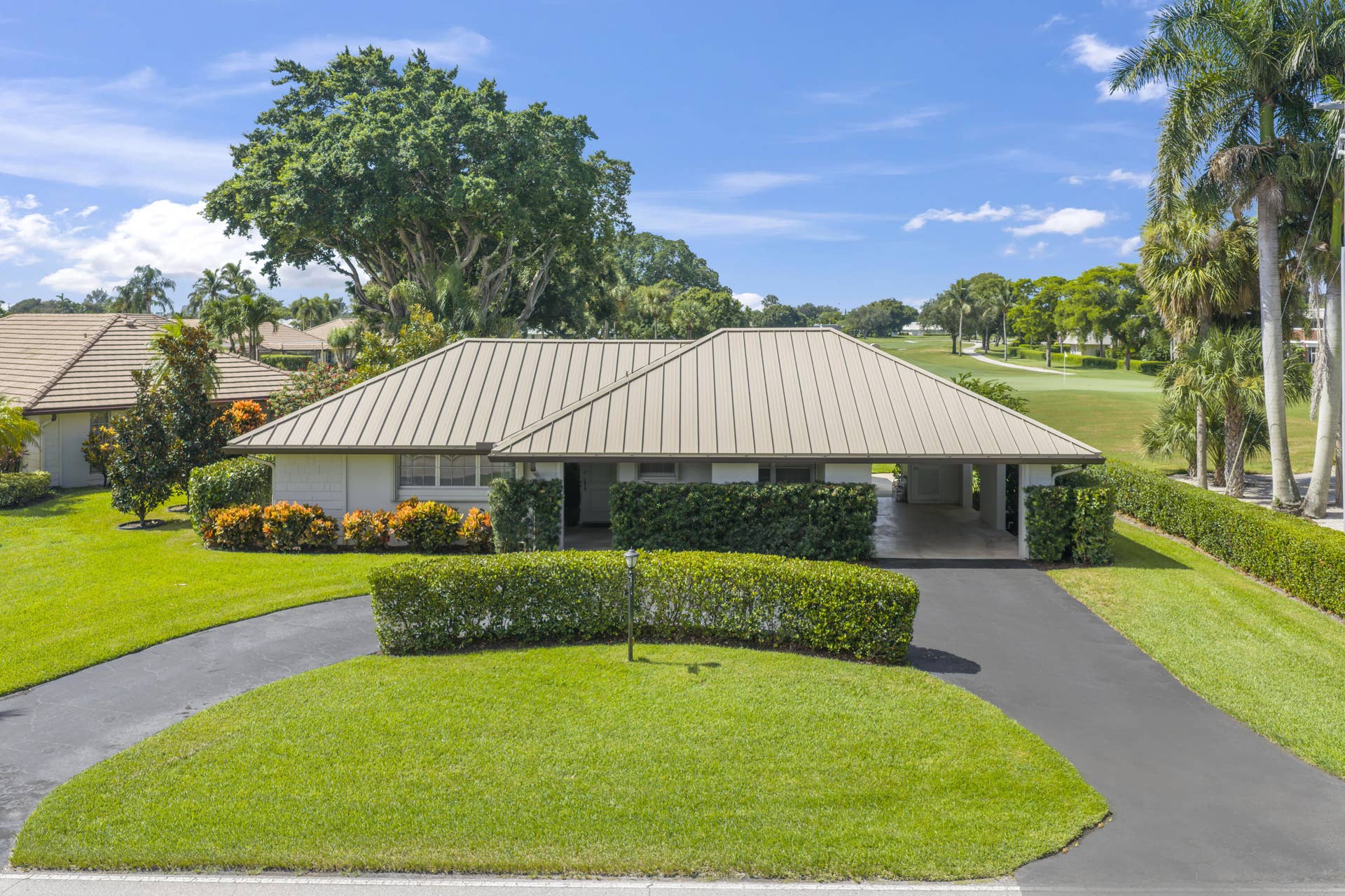 137 Clubhouse Boulevard, Atlantis, FL 33462 Single-story residence featuring a standing-seam metal roof, attached carport, paved circular driveway, and manicured landscaping