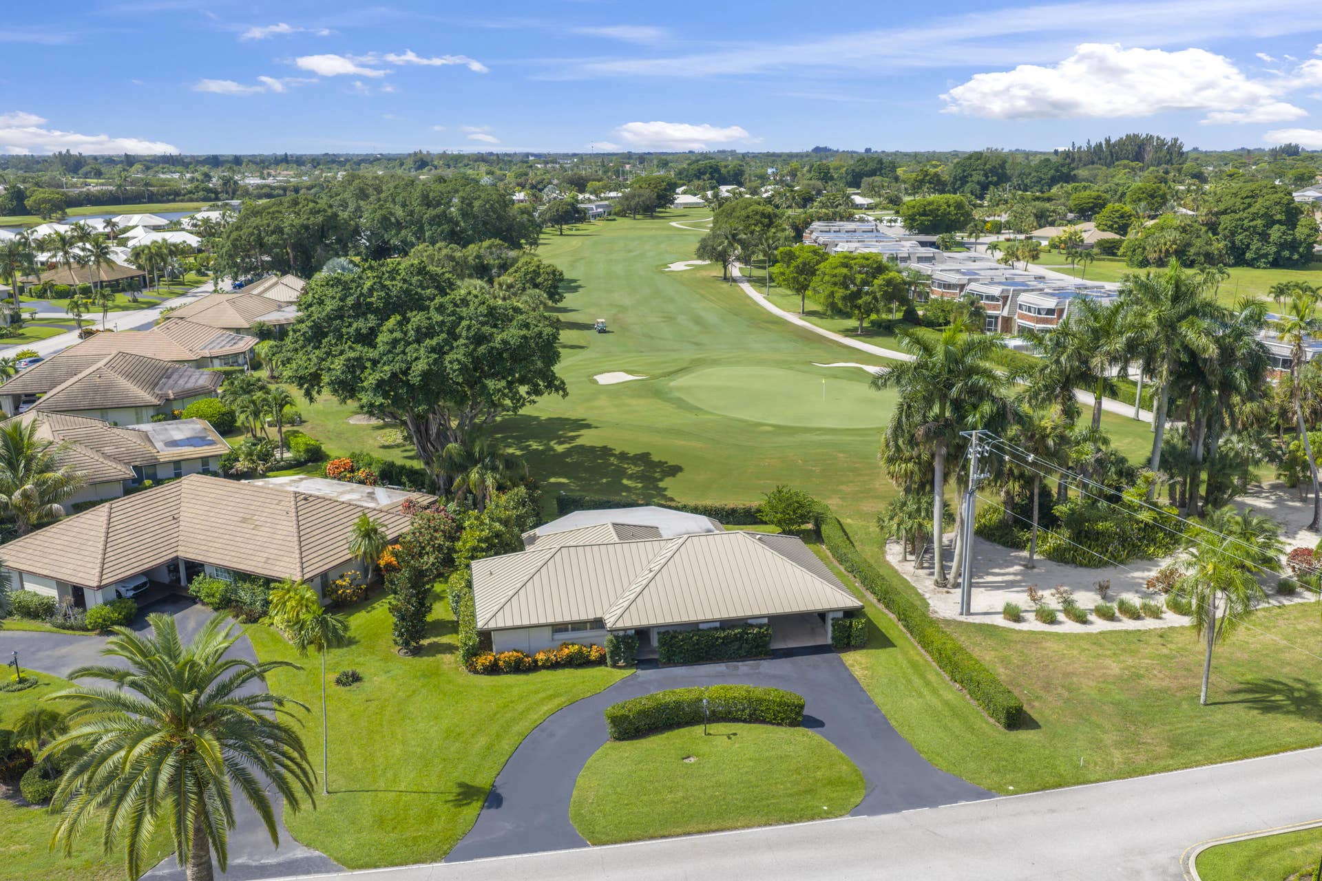 137 Clubhouse Boulevard, Atlantis, FL 33462 Aerial perspective featuring a single-story residence with a multi-hipped metal roof, curved asphalt driveway, and manicured lawn, situated on a golf course fairway