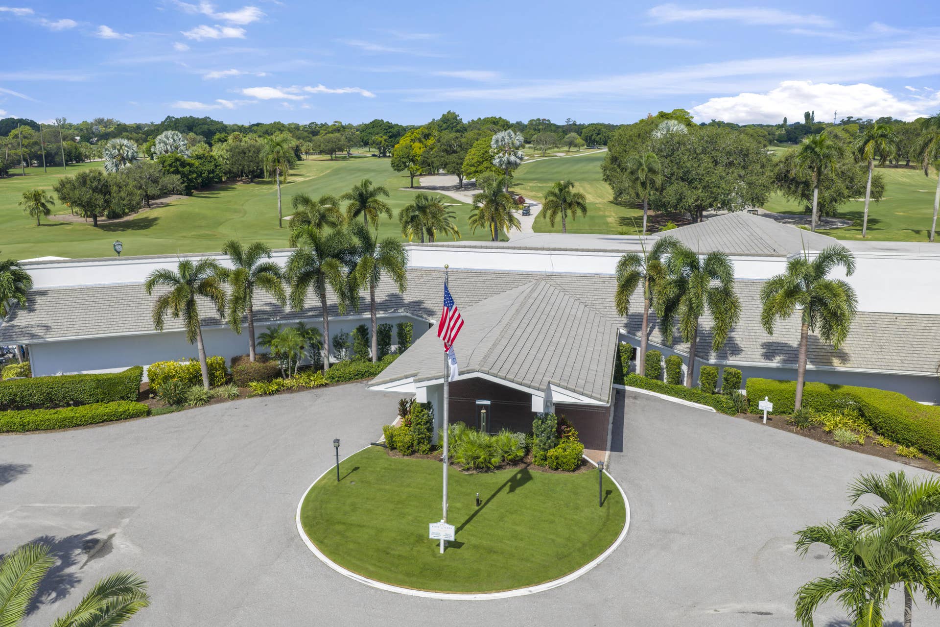 137 Clubhouse Boulevard, Atlantis, FL 33462 Asphalt porte-cochre entrance with a circular driveway and manicured lawn roundabout, featuring a metal roofline and professional landscaping