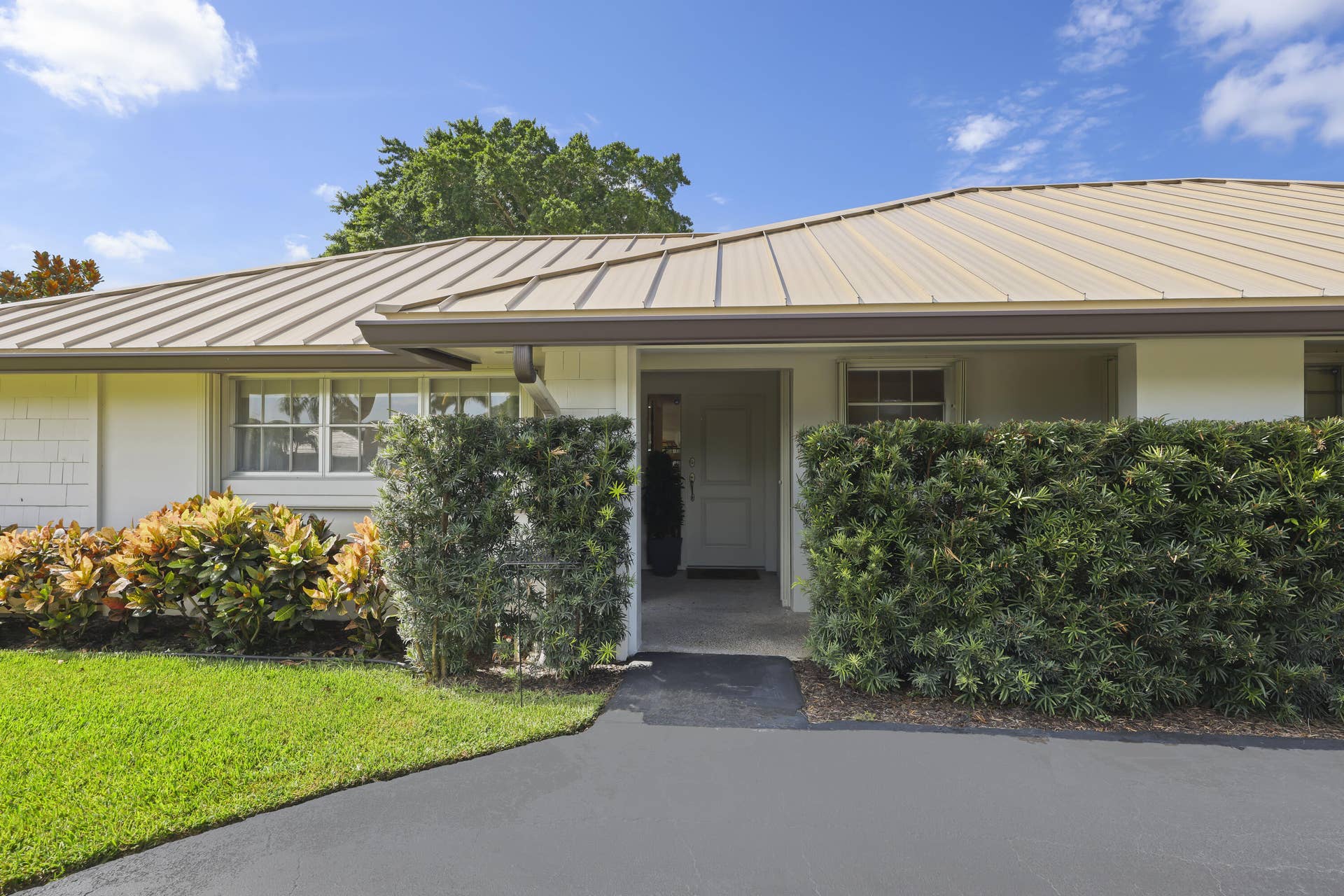 137 Clubhouse Boulevard, Atlantis, FL 33462 Exterior facade featuring a standing-seam metal roof, crisp white masonry walls, a recessed entryway, and manicured shrubbery