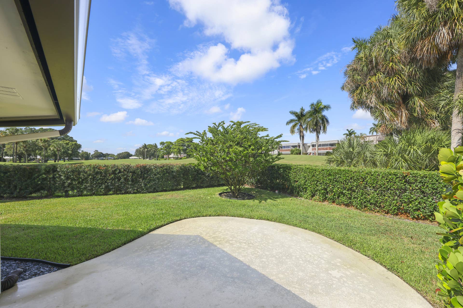 137 Clubhouse Boulevard, Atlantis, FL 33462 Concrete patio overlooking a manicured lawn, hedge-lined perimeter, and mature landscaping