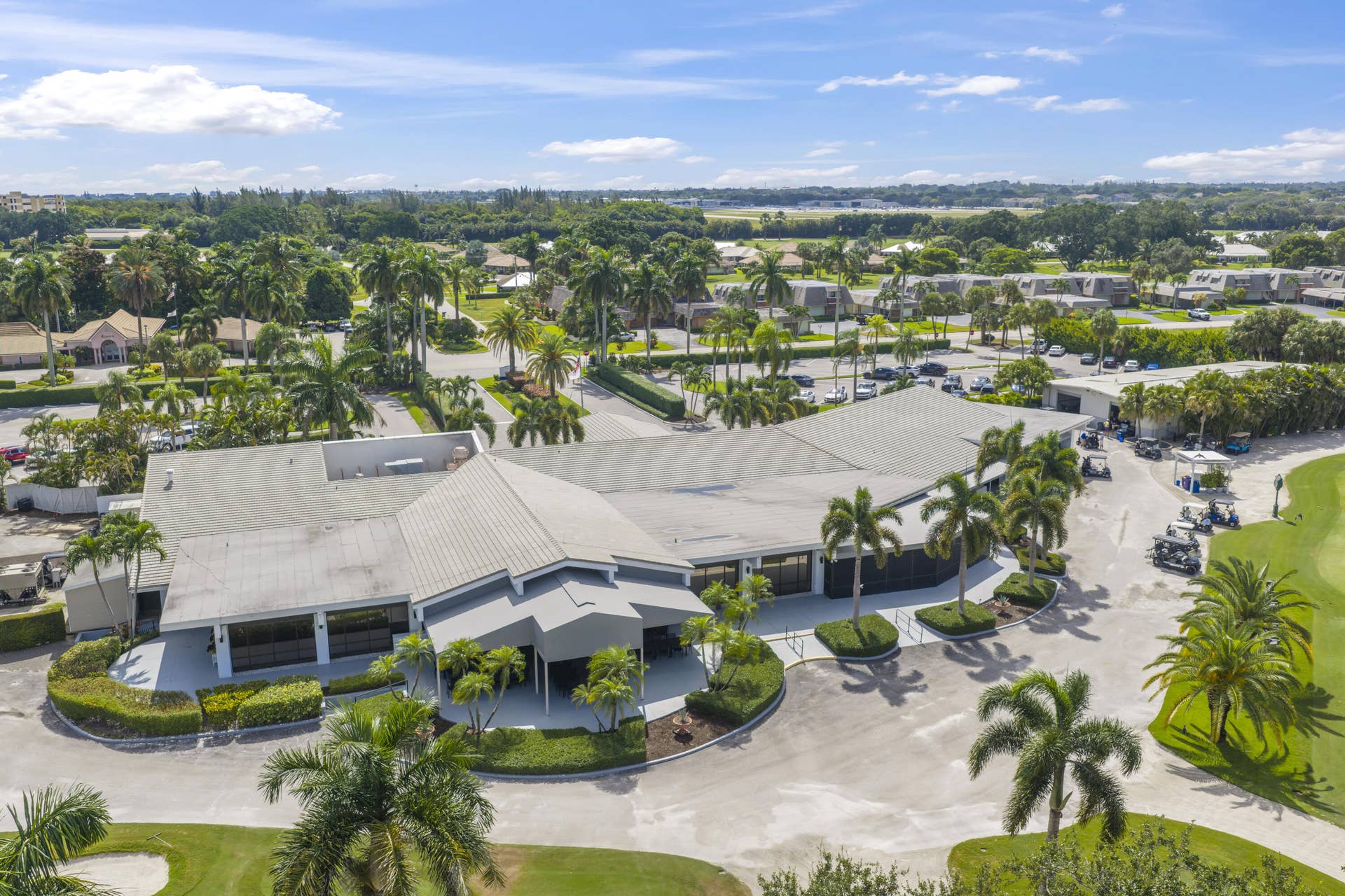 137 Clubhouse Boulevard, Atlantis, FL 33462 Aerial view of a sprawling clubhouse featuring a multi-gabled roof, covered entrance portico, and direct course-side positioning