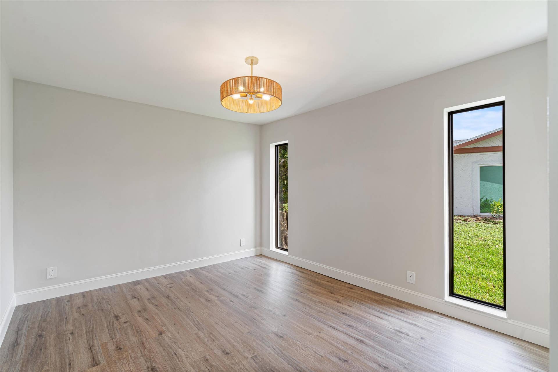 6111 WHITE OAK Lane, Tamarac, FL 33319 Neutral-toned room featuring wood-finish flooring, two vertical windows with black frames, and a drum-style pendant light fixture