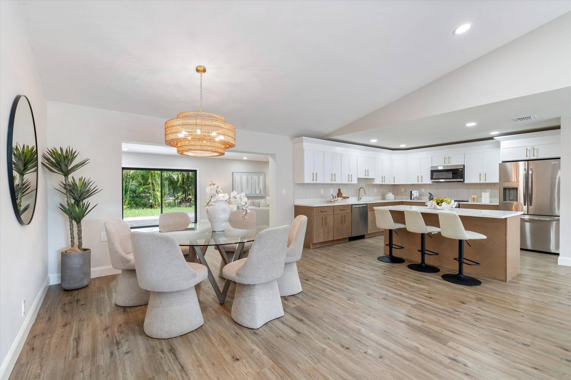 6111 WHITE OAK Lane, Tamarac, FL 33319 Kitchen featuring wood-finish cabinetry, white upper cabinets, stainless steel appliances, and a central island with a quartz countertop, complemented by wood-finish flooring and a vaulted ceiling