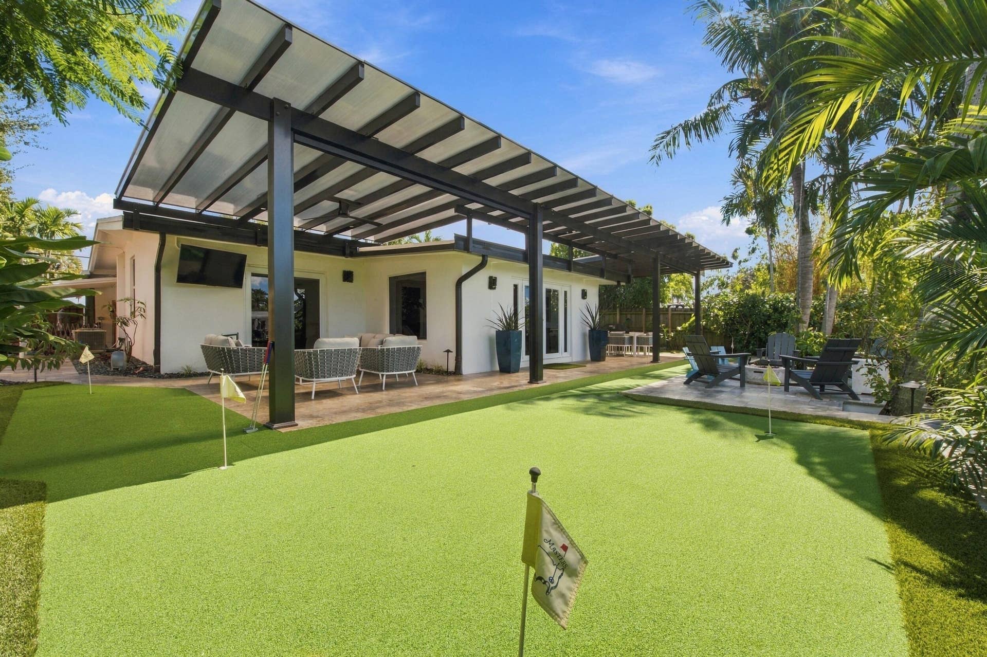2449 KEY LARGO Lane, Fort Lauderdale, FL 33312 Backyard featuring a synthetic turf putting green with multiple holes, covered patio with black metal structural framing, and hardscaped stone flooring