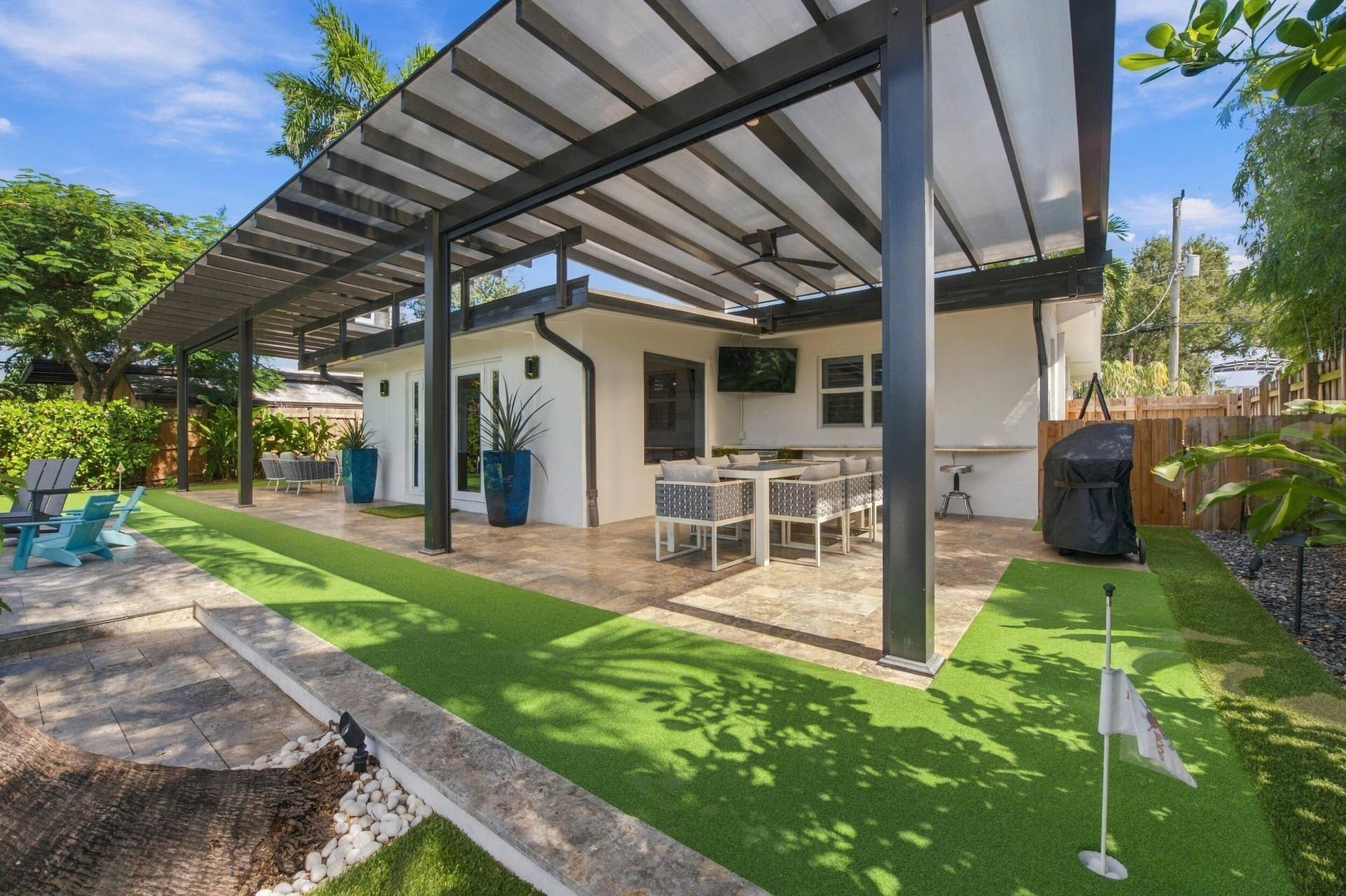 2449 KEY LARGO Lane, Fort Lauderdale, FL 33312 Covered outdoor patio featuring an overhead metal pergola, stone flooring, a built-in stone bar counter, and a putting green
