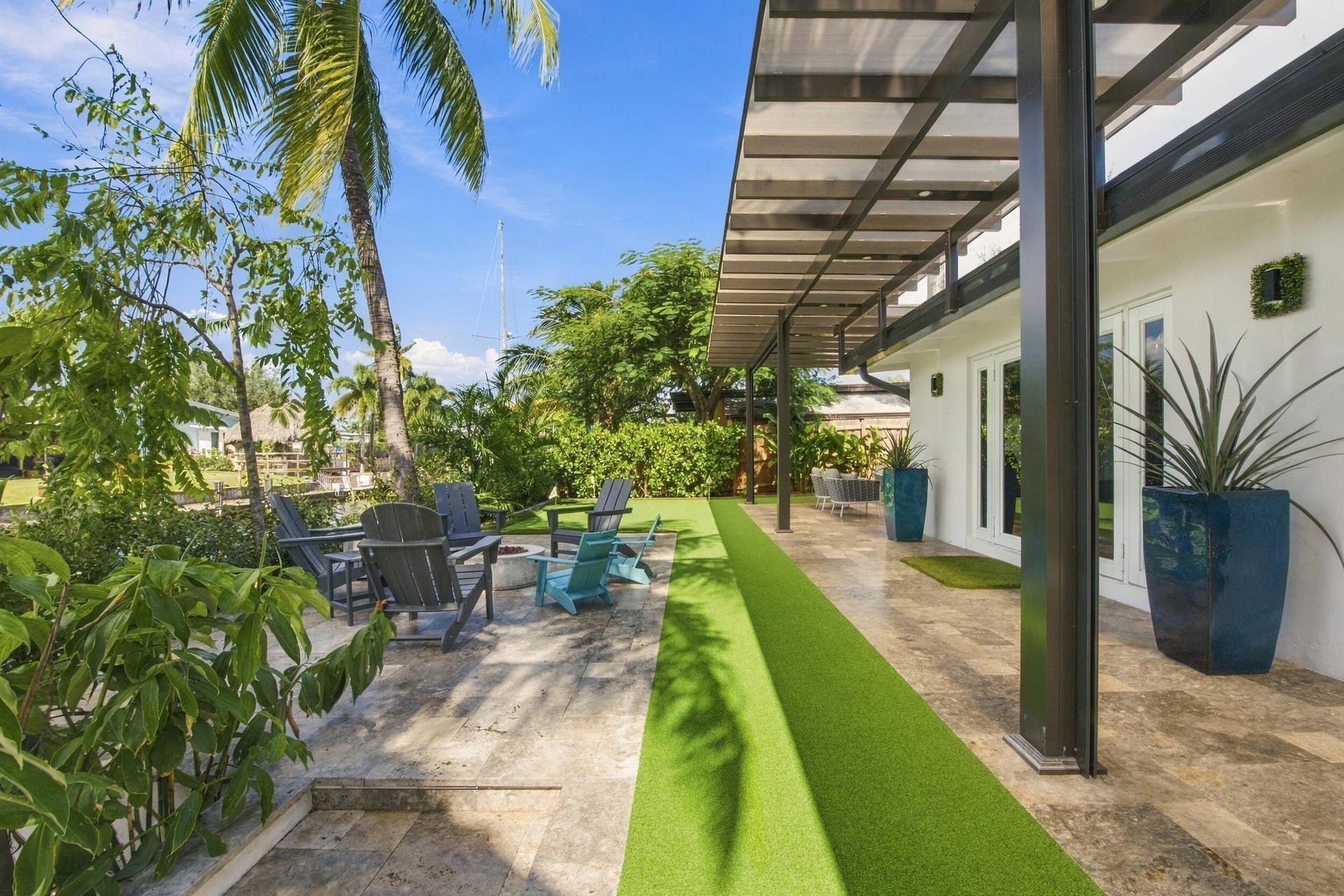 2449 KEY LARGO Lane, Fort Lauderdale, FL 33312 Covered patio featuring stone tile flooring and a metal-frame pergola, complemented by an outdoor area with stone hardscaping and a synthetic turf lawn
