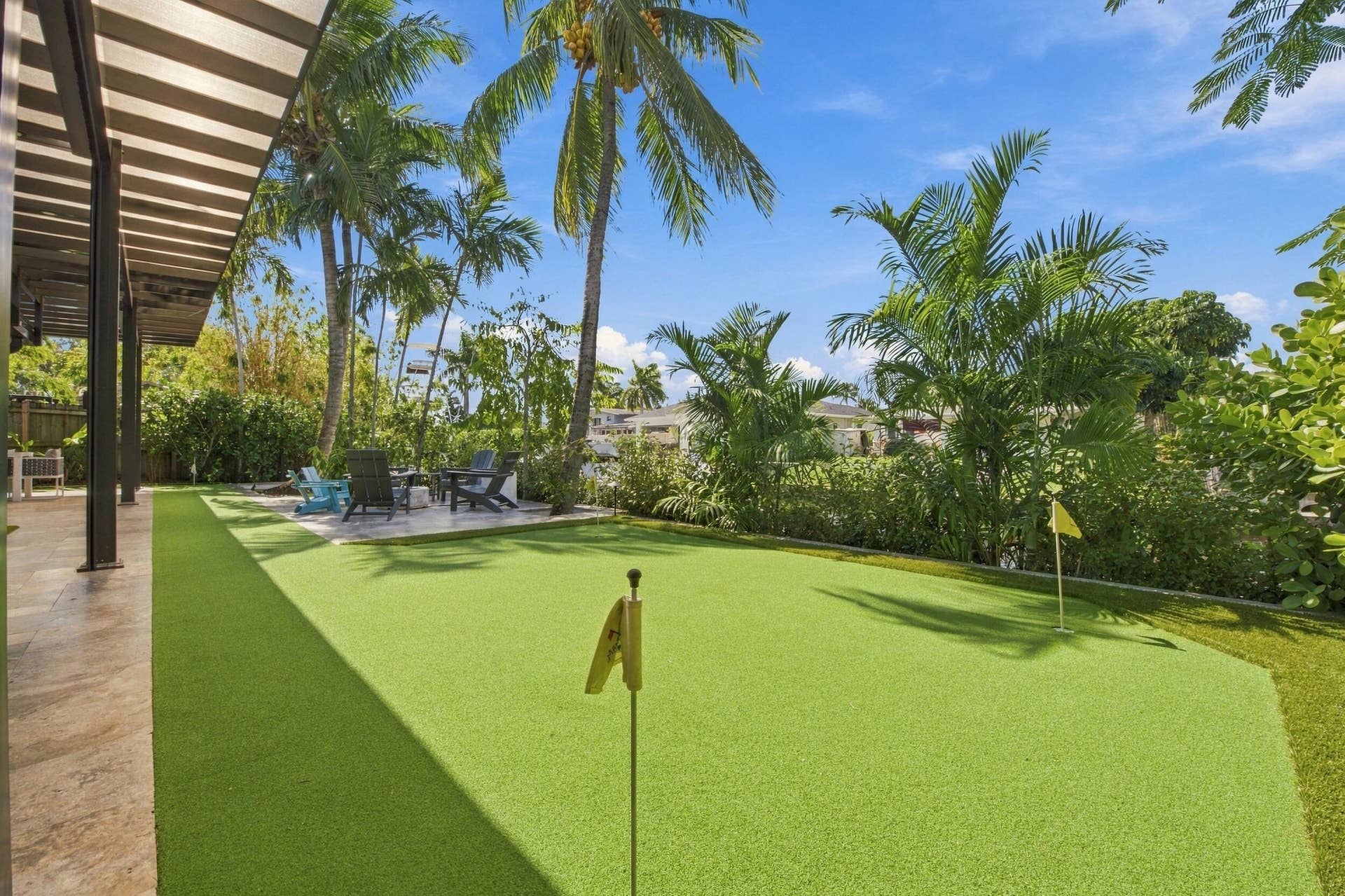 2449 KEY LARGO Lane, Fort Lauderdale, FL 33312 Backyard featuring a synthetic turf putting green, stone-tiled patio, covered veranda, and mature palm trees