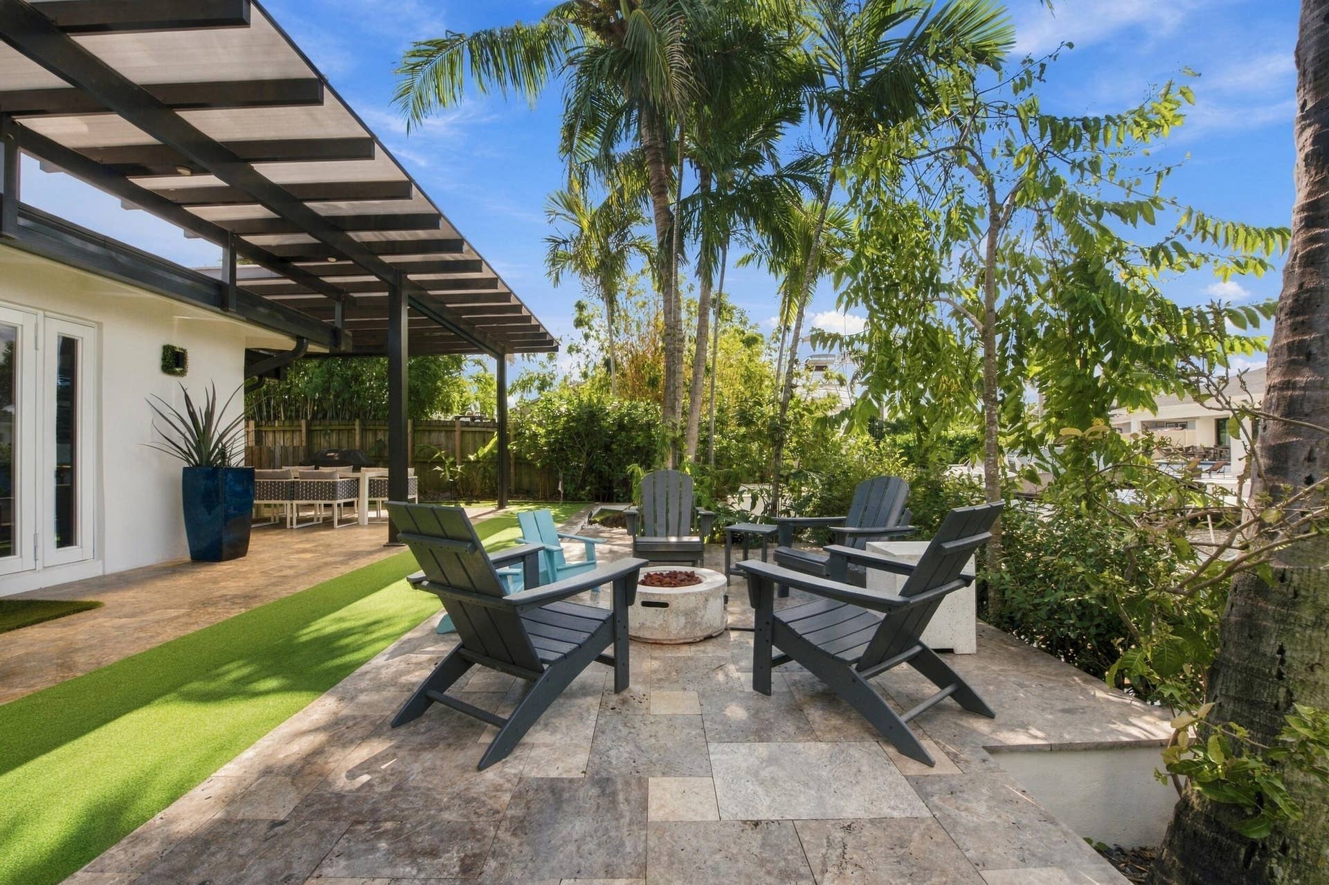 2449 KEY LARGO Lane, Fort Lauderdale, FL 33312 Patio area featuring natural stone pavers, a fixed metal-framed trellis, an integrated fire feature, and synthetic lawn accents