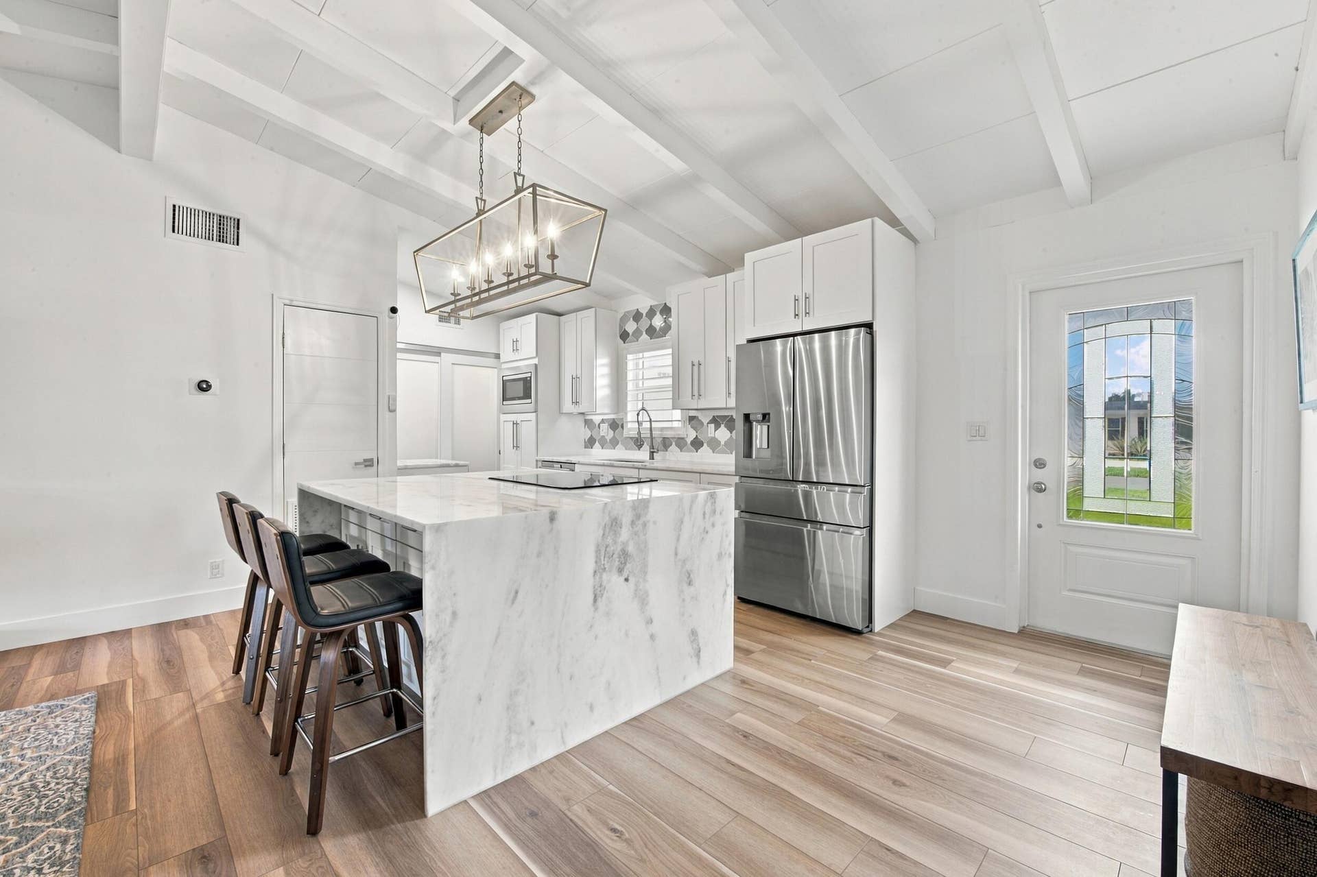 2449 KEY LARGO Lane, Fort Lauderdale, FL 33312 Kitchen featuring a waterfall-edge center island, wood-finish flooring, white shaker-style cabinetry, exposed ceiling beams, and a geometric tile backsplash