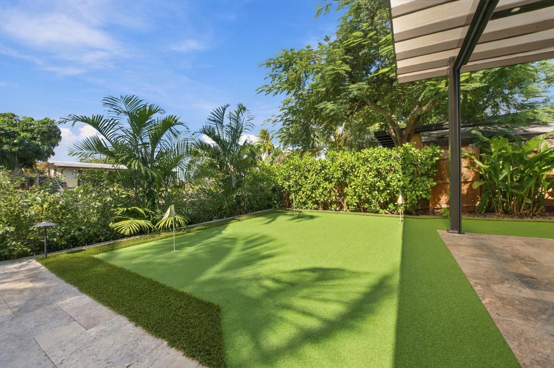 2449 KEY LARGO Lane, Fort Lauderdale, FL 33312 Backyard putting green featuring synthetic turf, stone-paver patio, metal structural awning, and privacy hedging