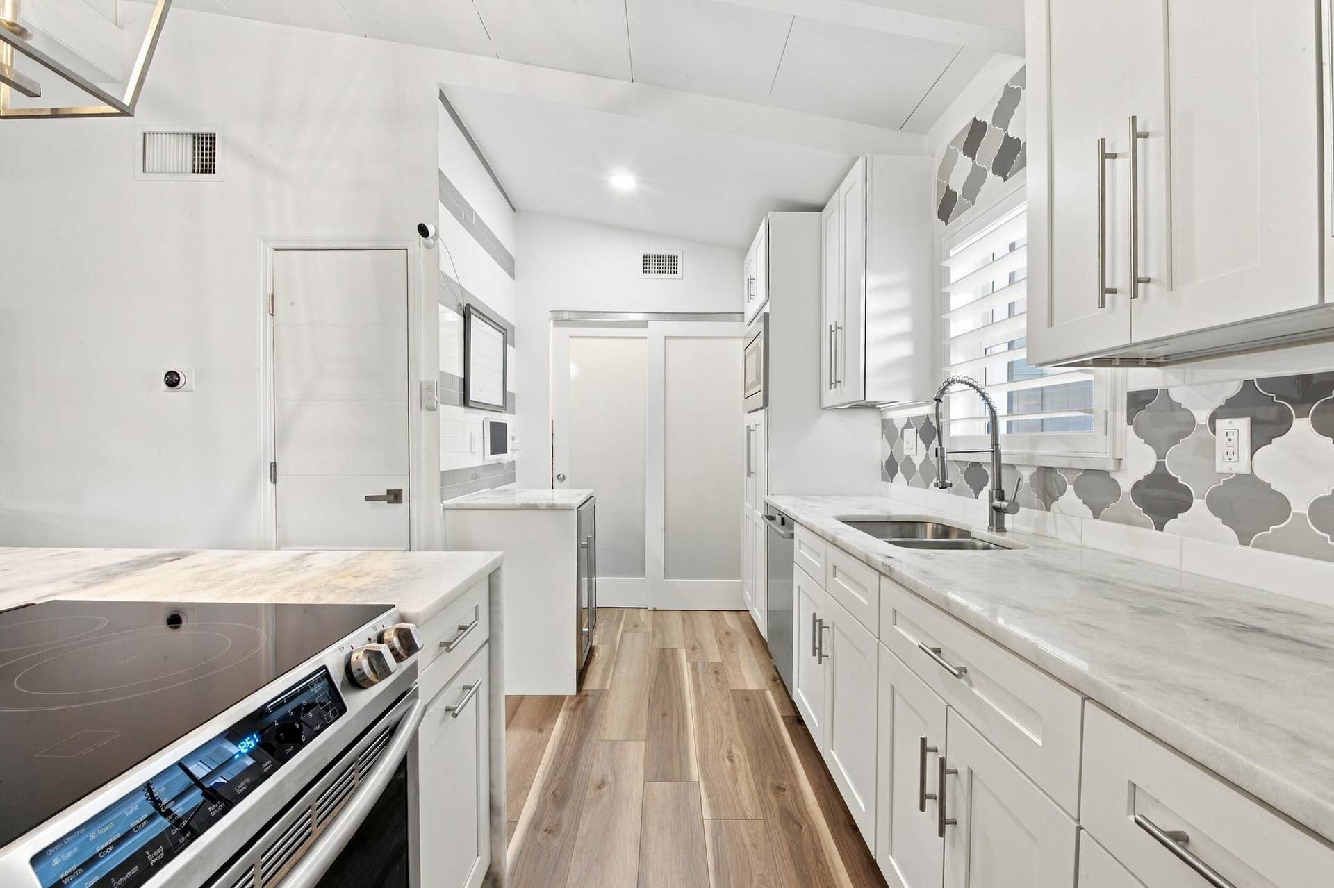 2449 KEY LARGO Lane, Fort Lauderdale, FL 33312 Kitchen featuring white cabinetry, stone-finish countertops, geometric tile backsplash, wood-finish flooring, and frosted glass sliding doors