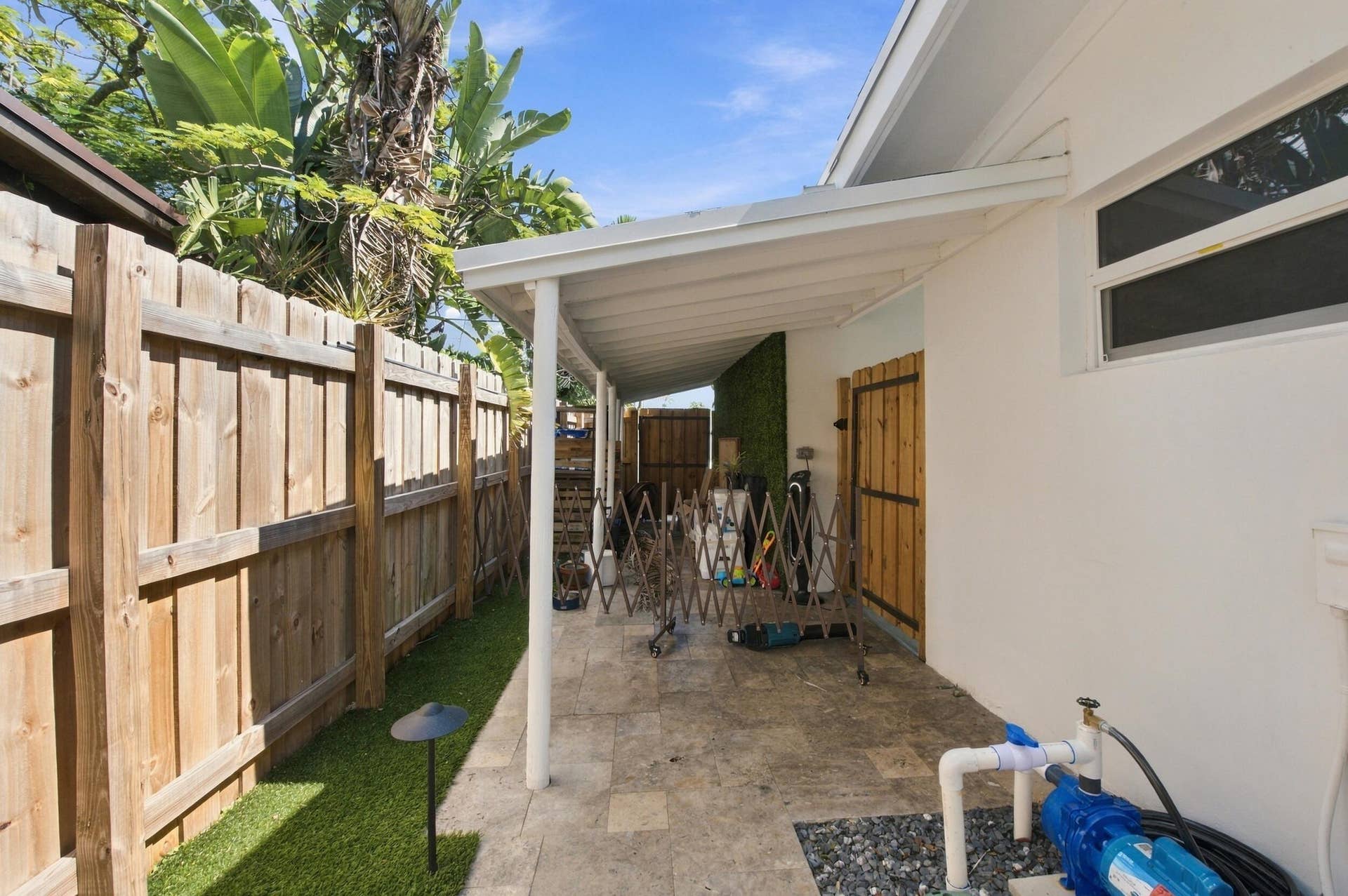 2449 KEY LARGO Lane, Fort Lauderdale, FL 33312 Covered patio featuring stone tile flooring, enclosed by a wood privacy fence, synthetic turf lawn, and a custom wood side gate