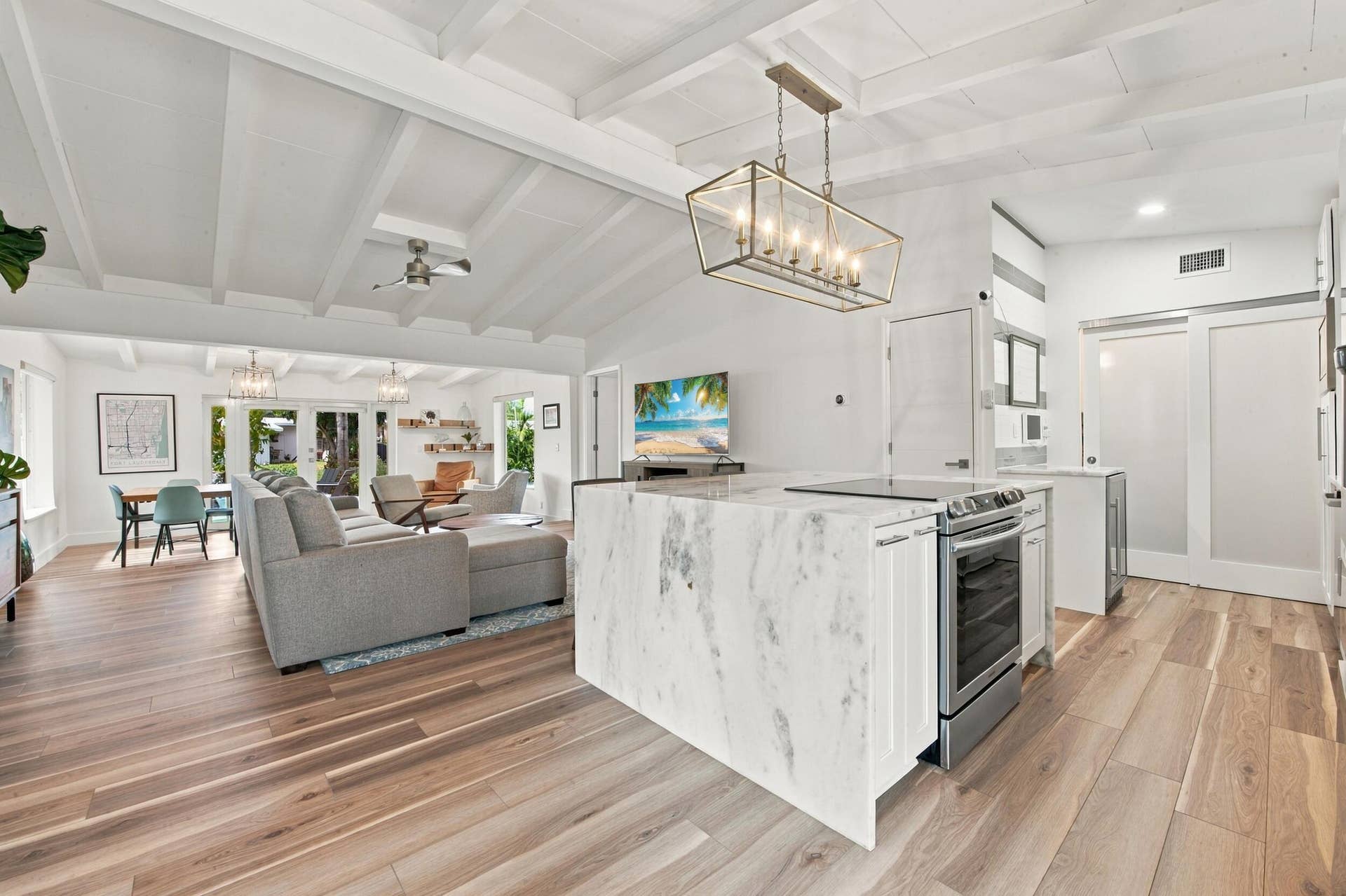 2449 KEY LARGO Lane, Fort Lauderdale, FL 33312 Kitchen island with stone-finish waterfall countertop, wood-finish flooring, exposed beam vaulted ceiling, and rectangular metal frame pendant lighting