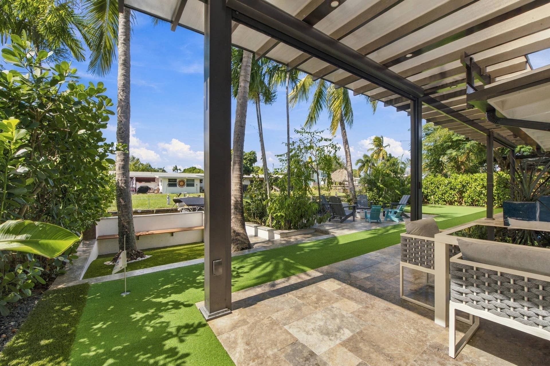 2449 KEY LARGO Lane, Fort Lauderdale, FL 33312 Covered patio featuring stone-tile flooring, louvered overhead structure, synthetic turf yard, built-in masonry seating, and mature palm trees