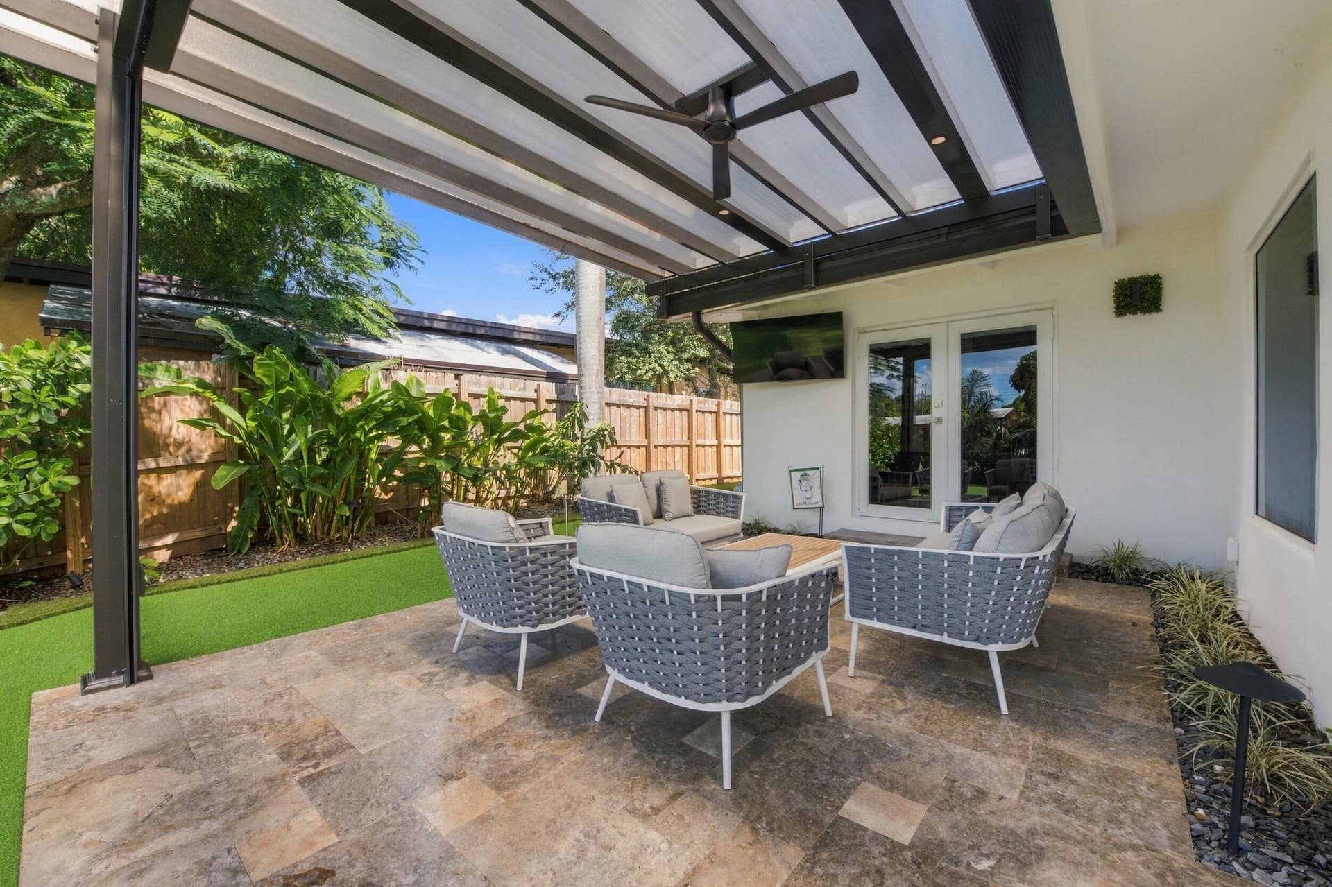 2449 KEY LARGO Lane, Fort Lauderdale, FL 33312 Covered outdoor patio featuring large-format stone tiling, a fixed overhead pergola, a built-in ceiling fan, and synthetic turf lawn
