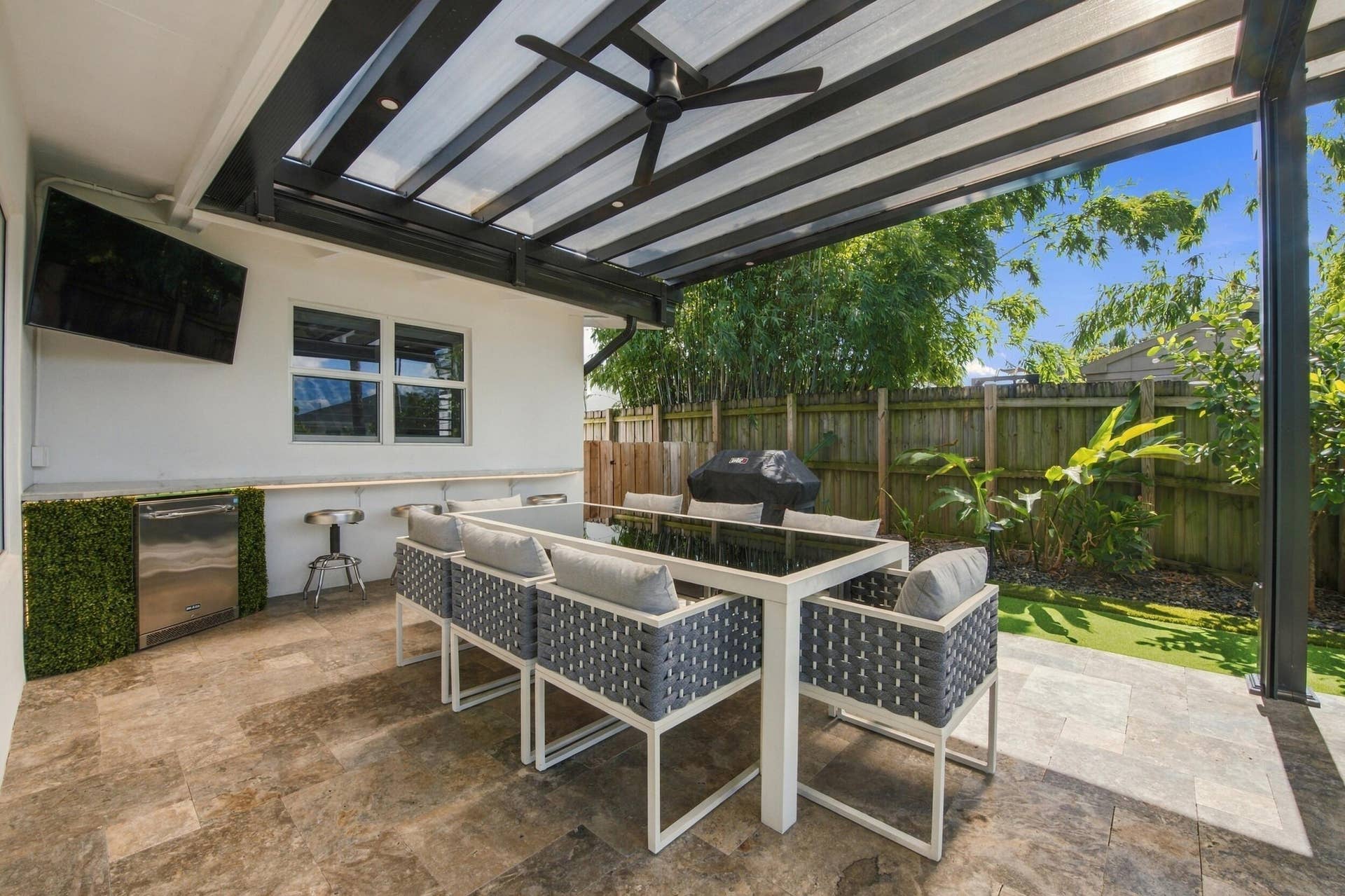 2449 KEY LARGO Lane, Fort Lauderdale, FL 33312 Covered patio featuring stone tile flooring, a built-in outdoor kitchen counter with an under-counter refrigerator, a black metal pergola, and a ceiling fan