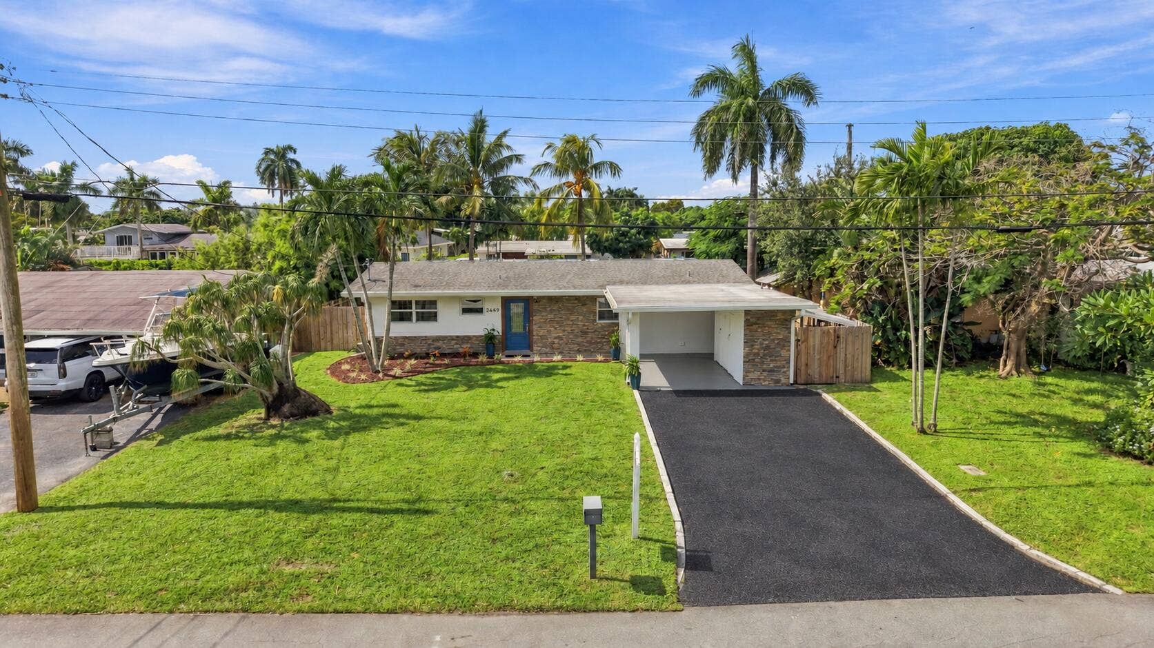 2449 KEY LARGO Lane, Fort Lauderdale, FL 33312 Single-story exterior featuring stone veneer facade, paved driveway, attached carport, and manicured landscaping