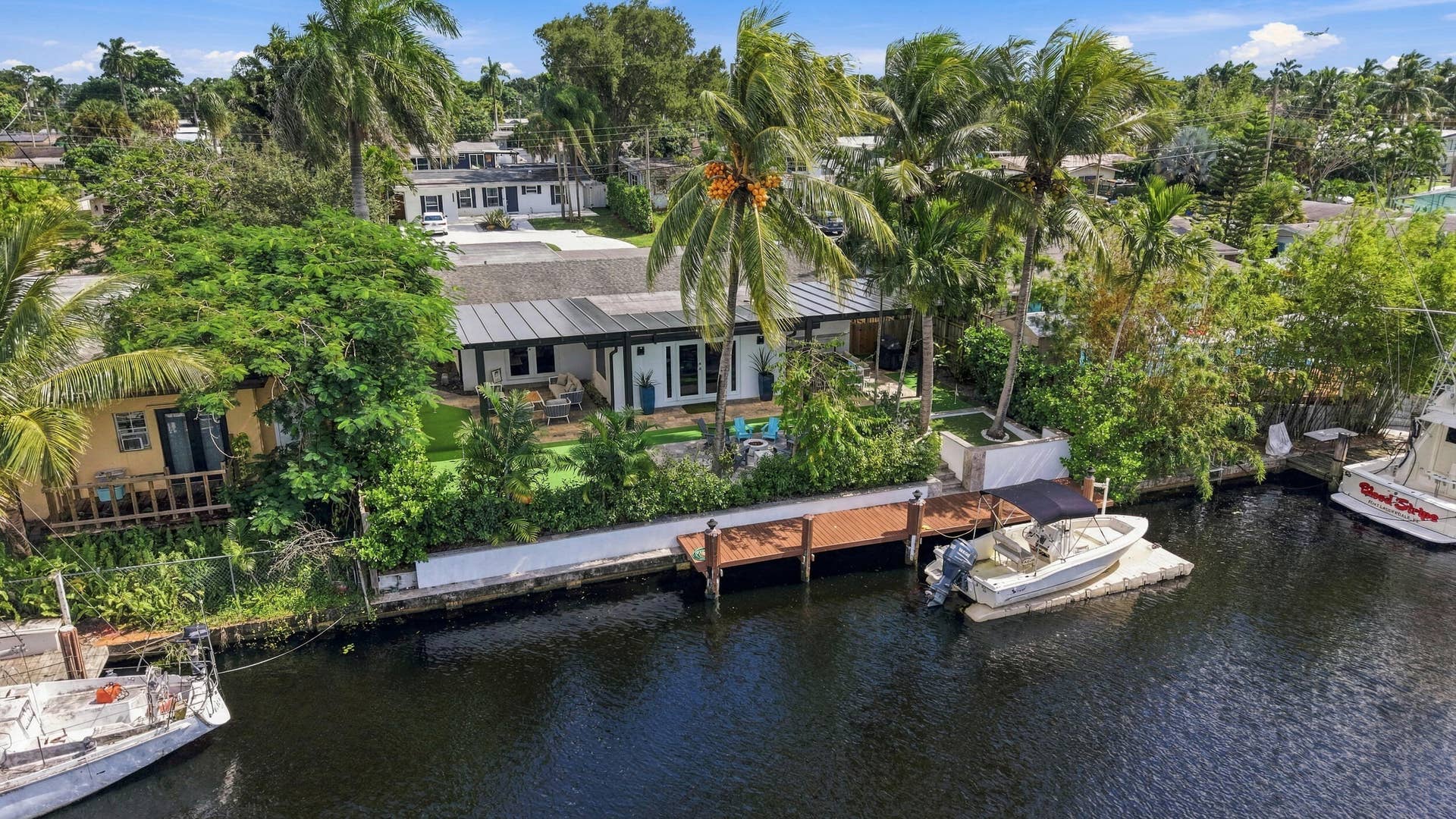 2449 KEY LARGO Lane, Fort Lauderdale, FL 33312 Waterfront property featuring a private wooden dock, a metal-seam roof, mature palm trees, and a concrete bulkhead
