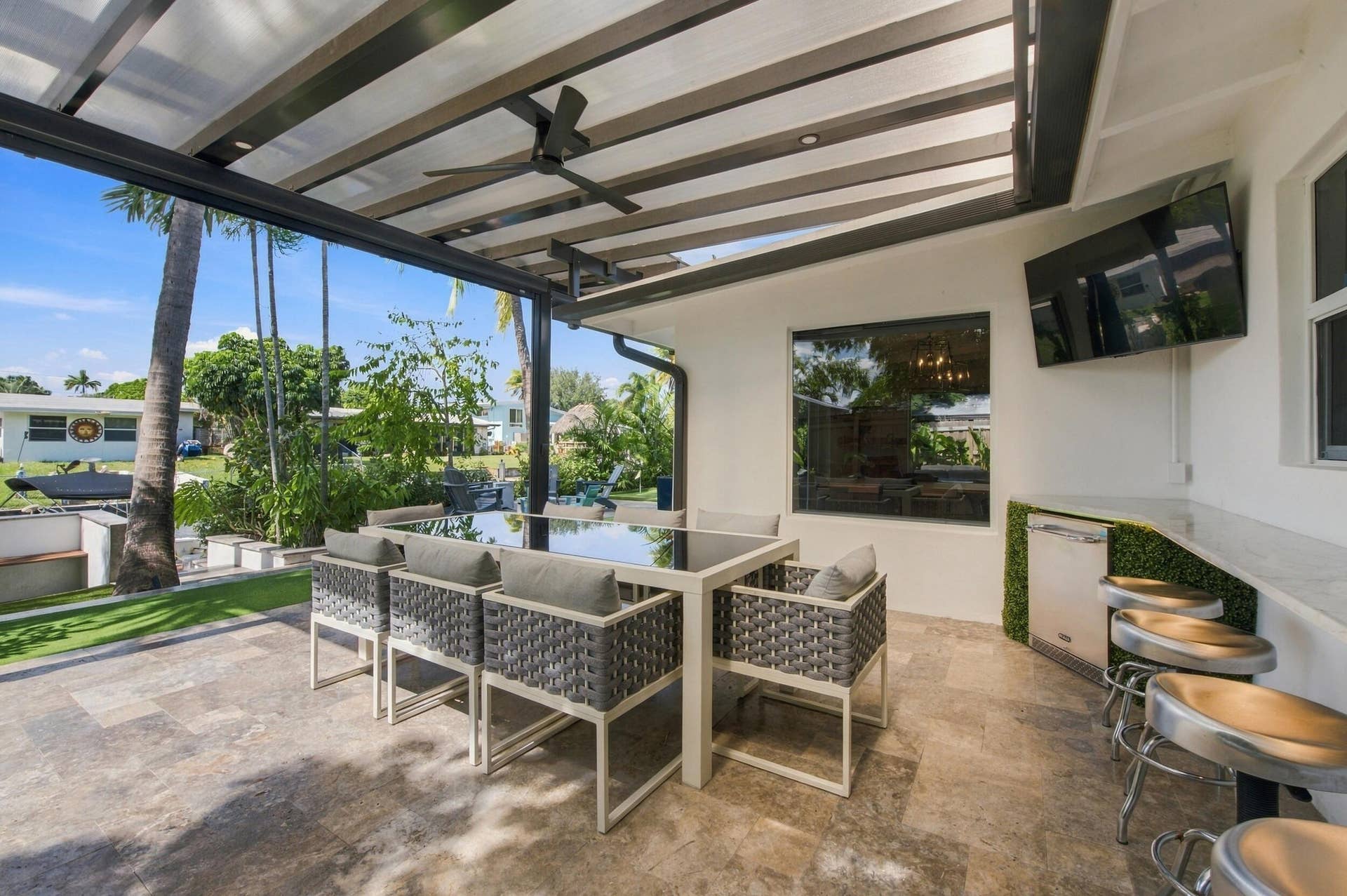 2449 KEY LARGO Lane, Fort Lauderdale, FL 33312 Covered patio featuring stone-tiled flooring, a slatted timber pergola, a built-in outdoor bar with a stone countertop, an integrated ceiling fan, and a mounted flat-screen television