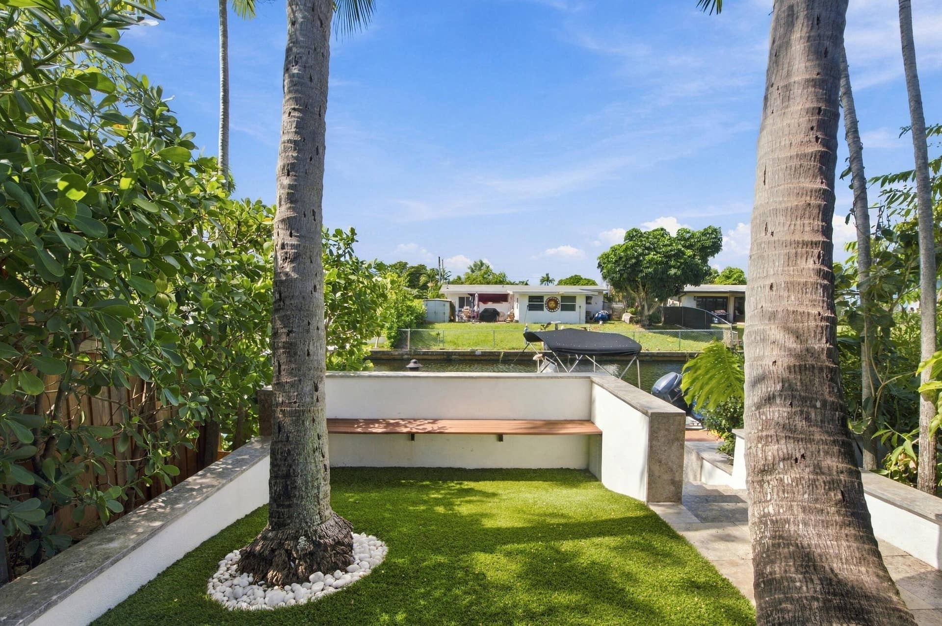 2449 KEY LARGO Lane, Fort Lauderdale, FL 33312 Waterfront outdoor space featuring a stone-capped perimeter wall, integrated wood-finish bench seating, synthetic turf ground cover, and mature palm trees