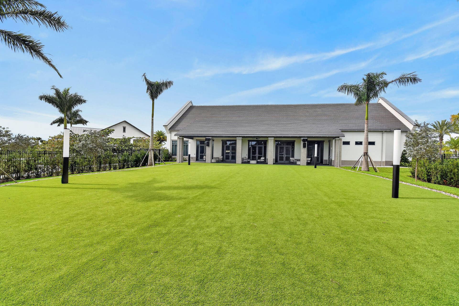 15811 Key Biscayne Lane, Westlake, FL 33470 Expansive green lawn with established palm trees, perimeter fencing, and a modern building with a dark-tiled roof and multiple glass doors