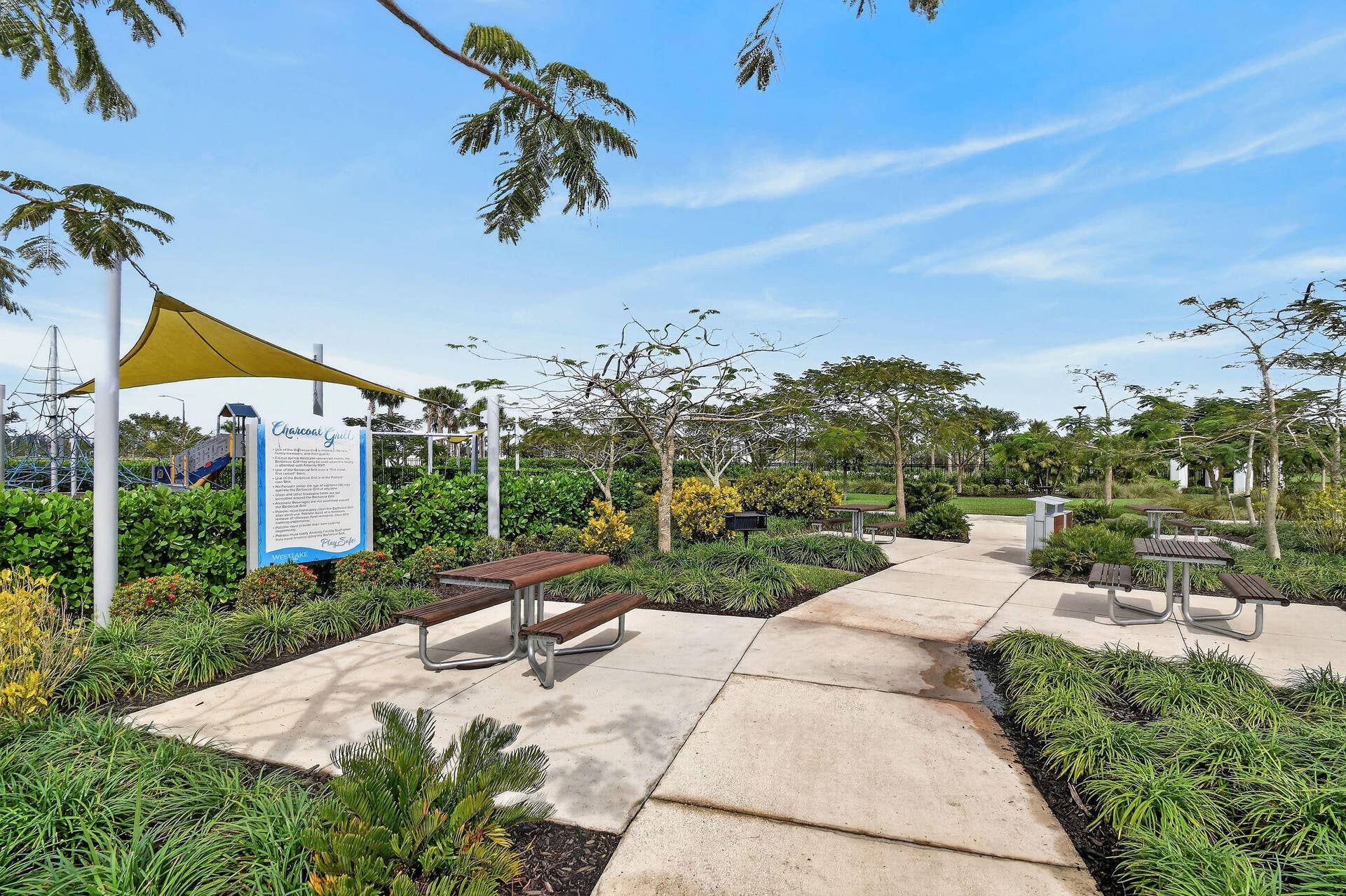 15811 Key Biscayne Lane, Westlake, FL 33470 Paved pathways traversing a landscaped park, featuring multiple picnic tables, a shade structure, and a prominent informational sign