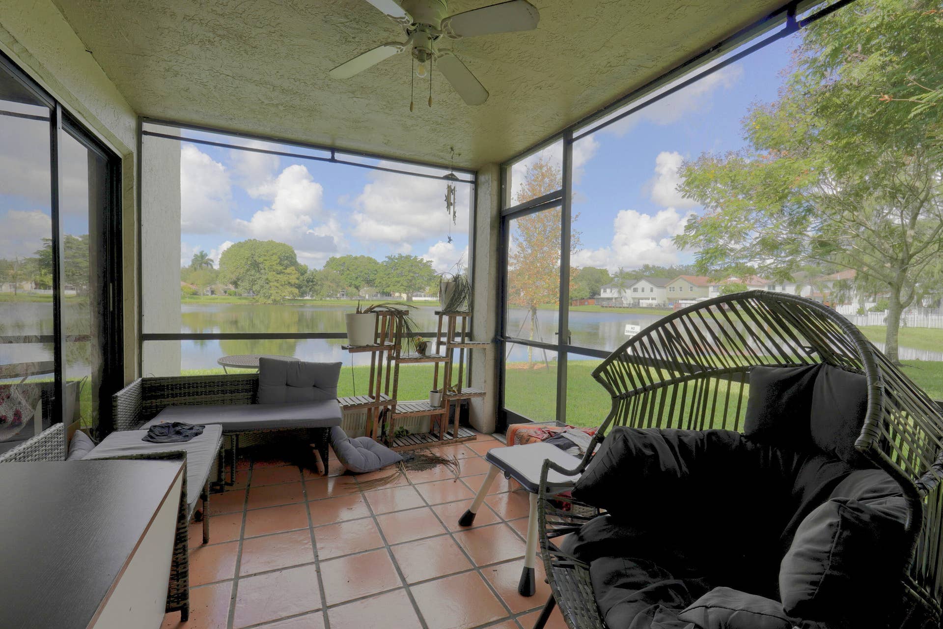 9853 NW 3RD Court, #7, Plantation, FL 33324 Screened lanai featuring tile flooring, a ceiling fan, and metal framing with full-height screens overlooking a lake