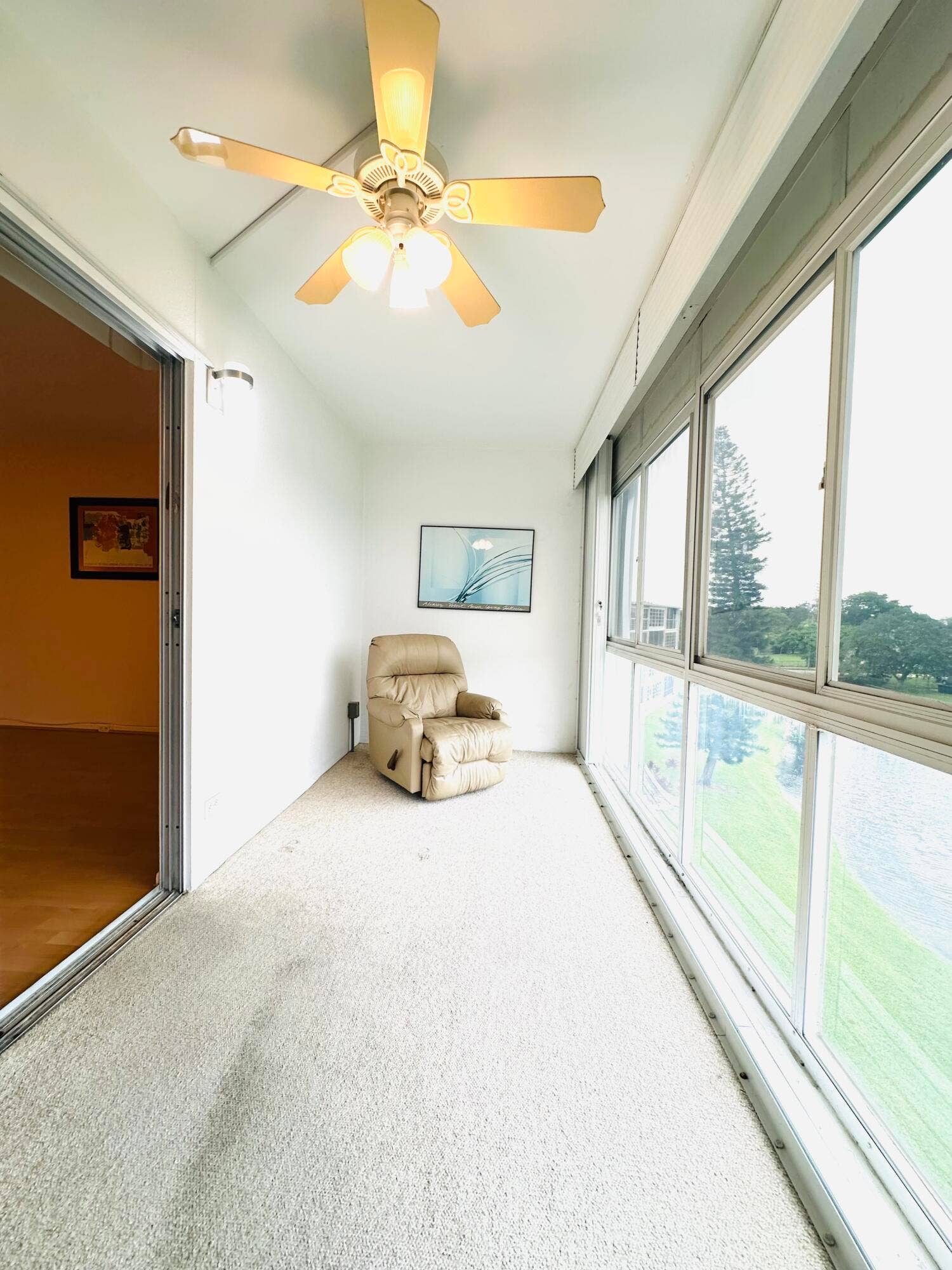 4011 NEWPORT G, Deerfield Beach, FL 33442 Enclosed porch featuring expansive multi-pane glass walls, carpeted flooring, and a ceiling-mounted light fixture with a three-blade fan