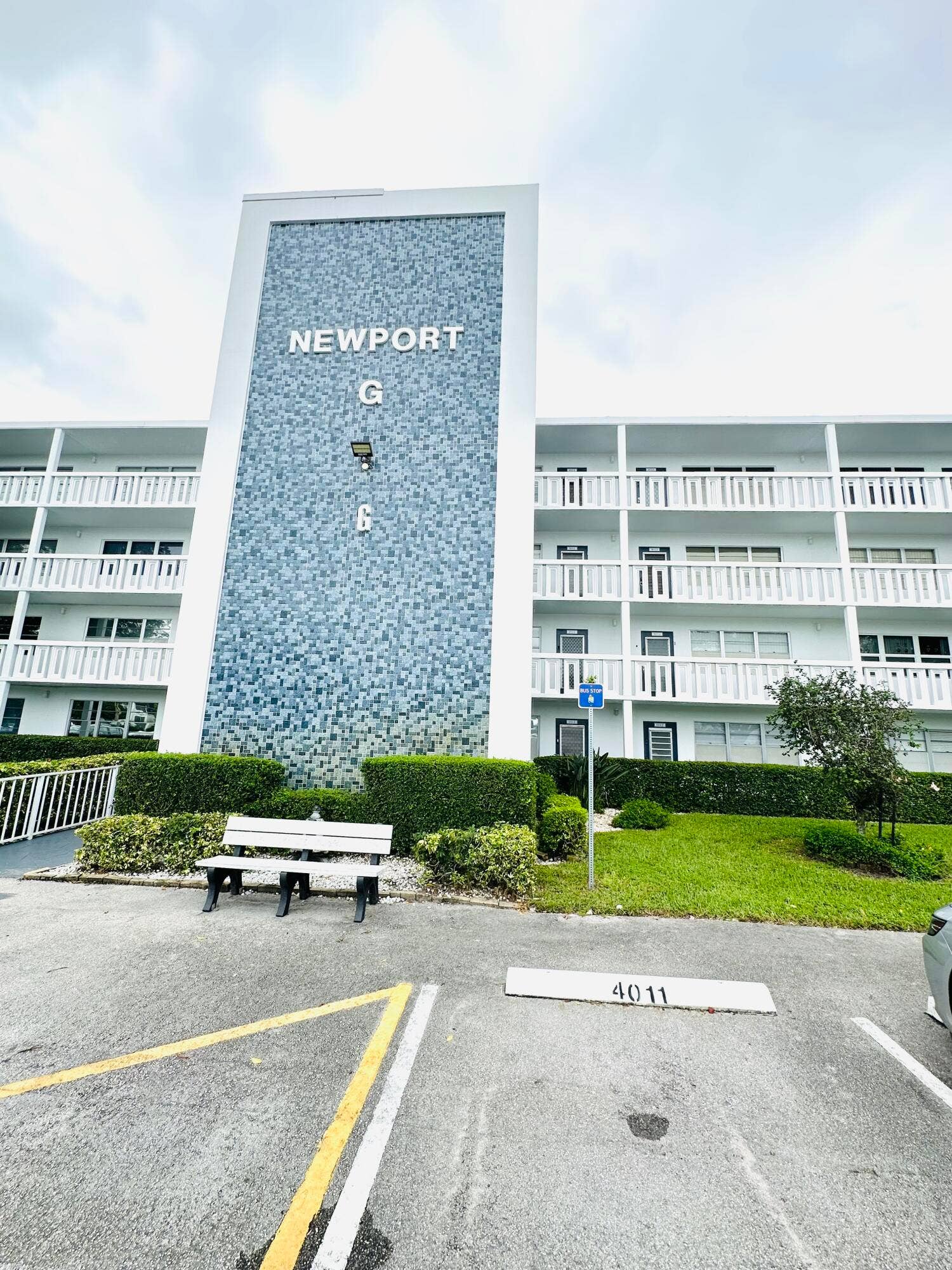 4011 NEWPORT G, Deerfield Beach, FL 33442 Multi-story building exterior featuring a decorative tile facade, tiered open-air balconies with white railings, and manicured shrubbery