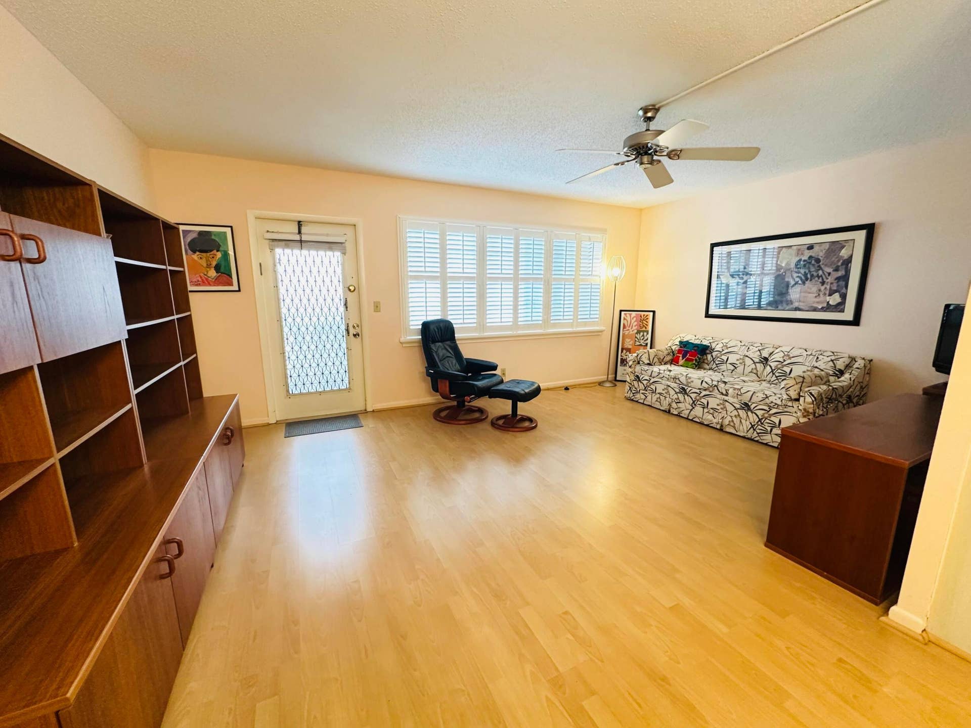 4011 NEWPORT G, Deerfield Beach, FL 33442 Living area featuring laminate flooring, wall unit, multi-panel window with white plantation-style shutters, and a ceiling fan