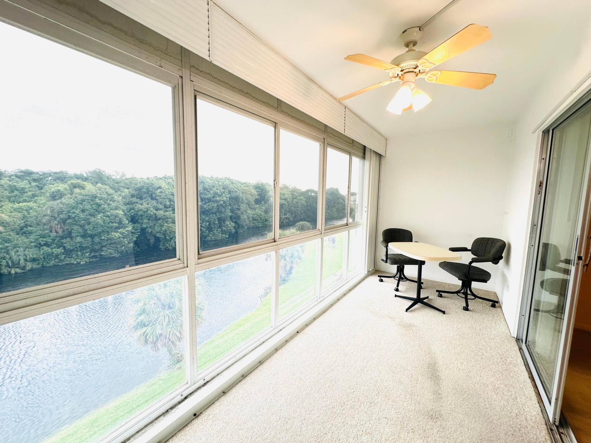 4011 NEWPORT G, Deerfield Beach, FL 33442 Enclosed sunroom featuring expansive floor-to-ceiling windows, water-facing exterior, textured flooring, and a ceiling-mounted light fixture with fan