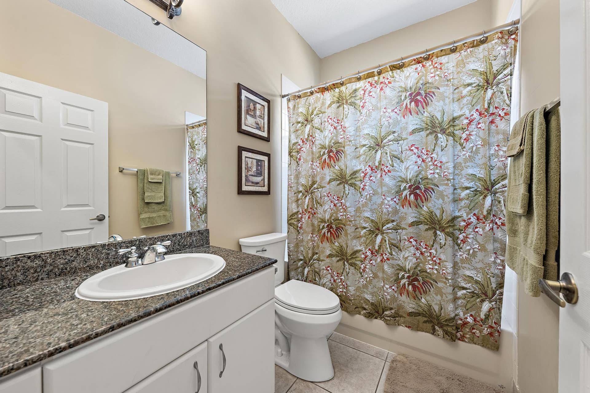 Bathroom featuring a vanity with a stone-finish countertop, white cabinetry, an oval undermount sink, a large wall-mounted mirror, and tile flooring