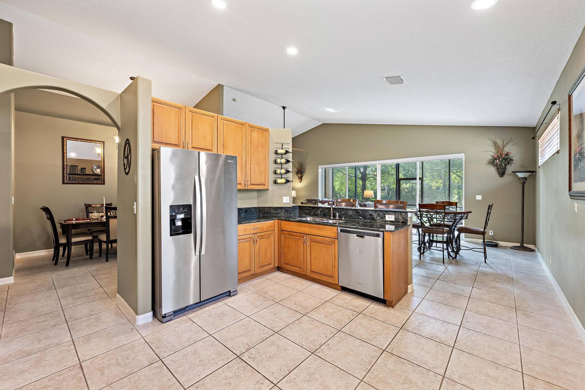 Kitchen featuring natural wood cabinetry, dark stone countertops, stainless steel appliances, tile flooring, and vaulted ceilings