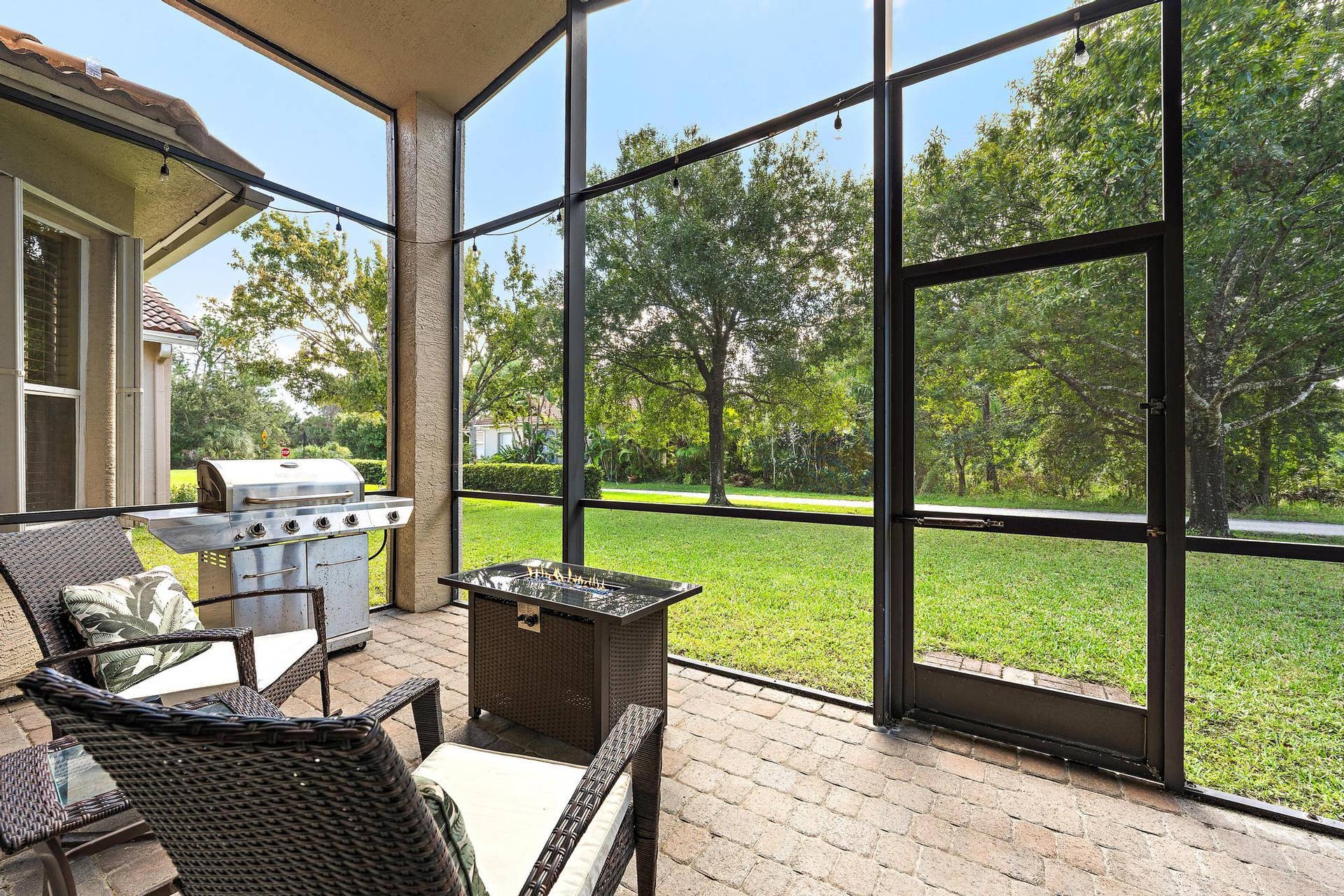 Screen-enclosed patio featuring paver flooring, built-in stainless steel grill, and expansive exterior green space