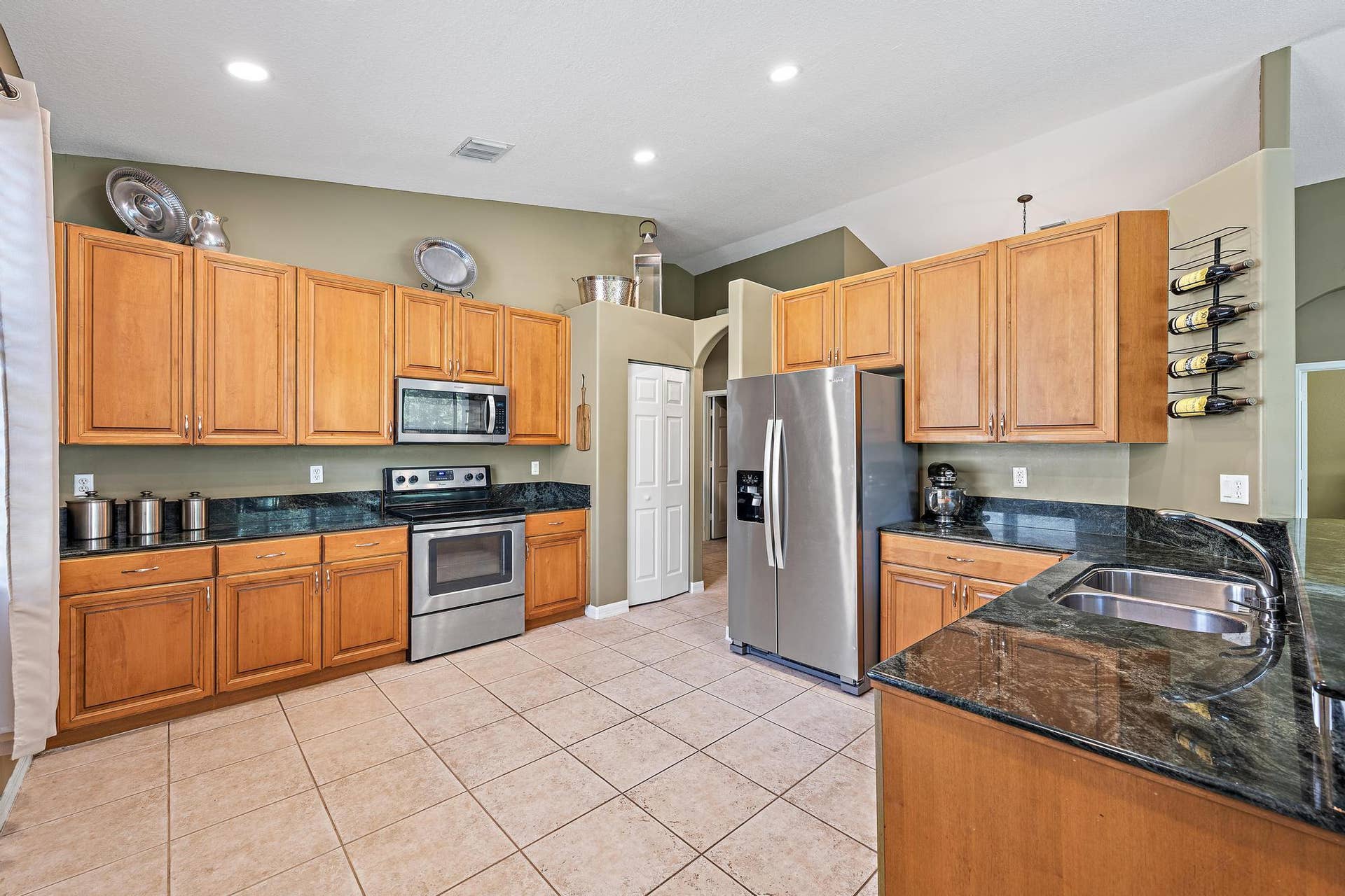 Kitchen featuring natural wood cabinetry, dark stone countertops, stainless steel appliances, a double-basin sink, and tile flooring