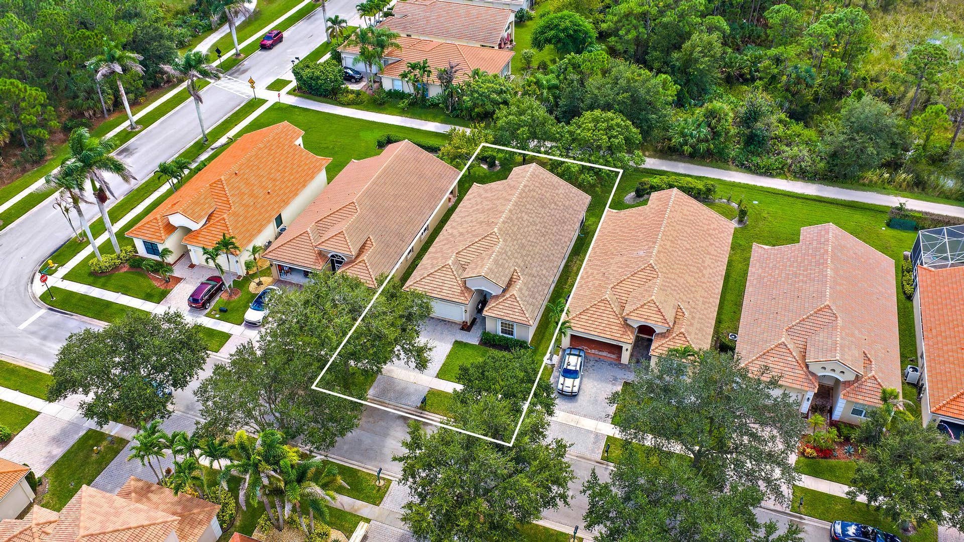 Single-story residence featuring tiled roof, paved driveway, two-car garage, and established landscaping