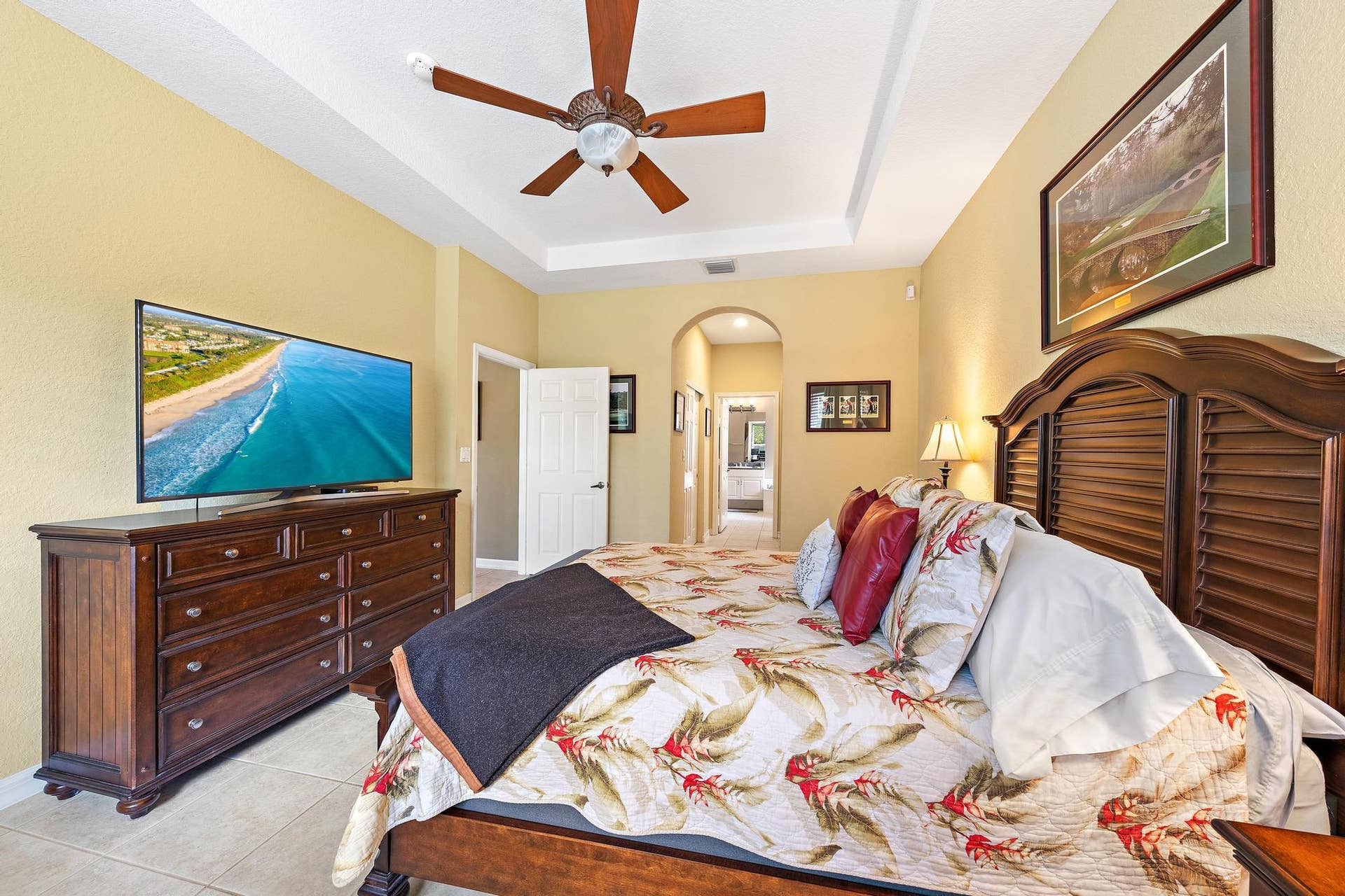 Bedroom featuring a tray ceiling, arched doorway, and neutral tile flooring