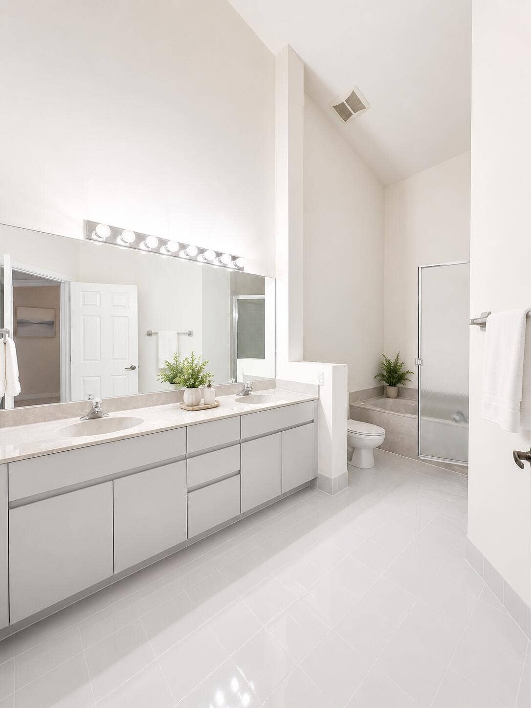 Double vanity featuring light-gray toned cabinetry, dual drop-in sinks, a large wall-spanning mirror, and high vaulted ceilings with a glass-enclosed shower and tub combination