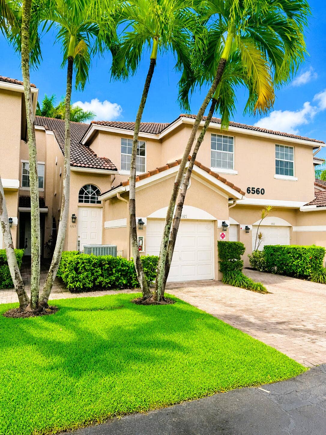 Two-story exterior featuring a stucco faade, a tiled roof, a paved driveway, and established palm tree landscaping