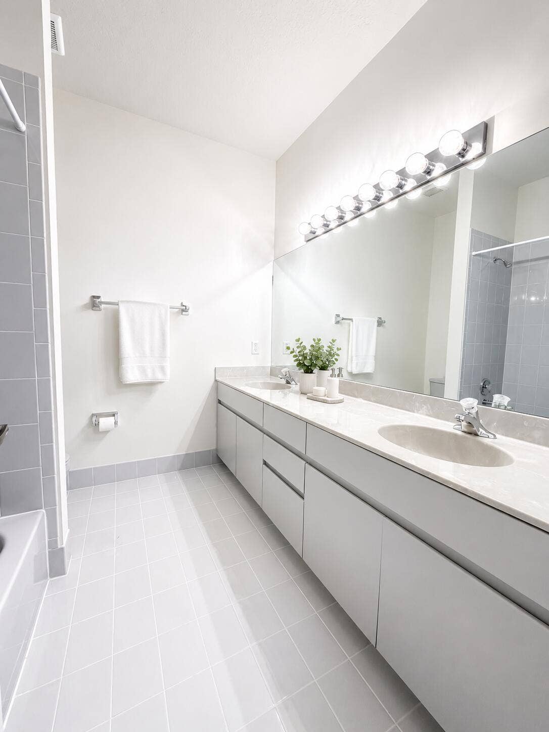 Double vanity featuring slab-front cabinetry, stone-finish countertops, undermount sinks, and a large-format vanity mirror with integrated multi-bulb lighting
