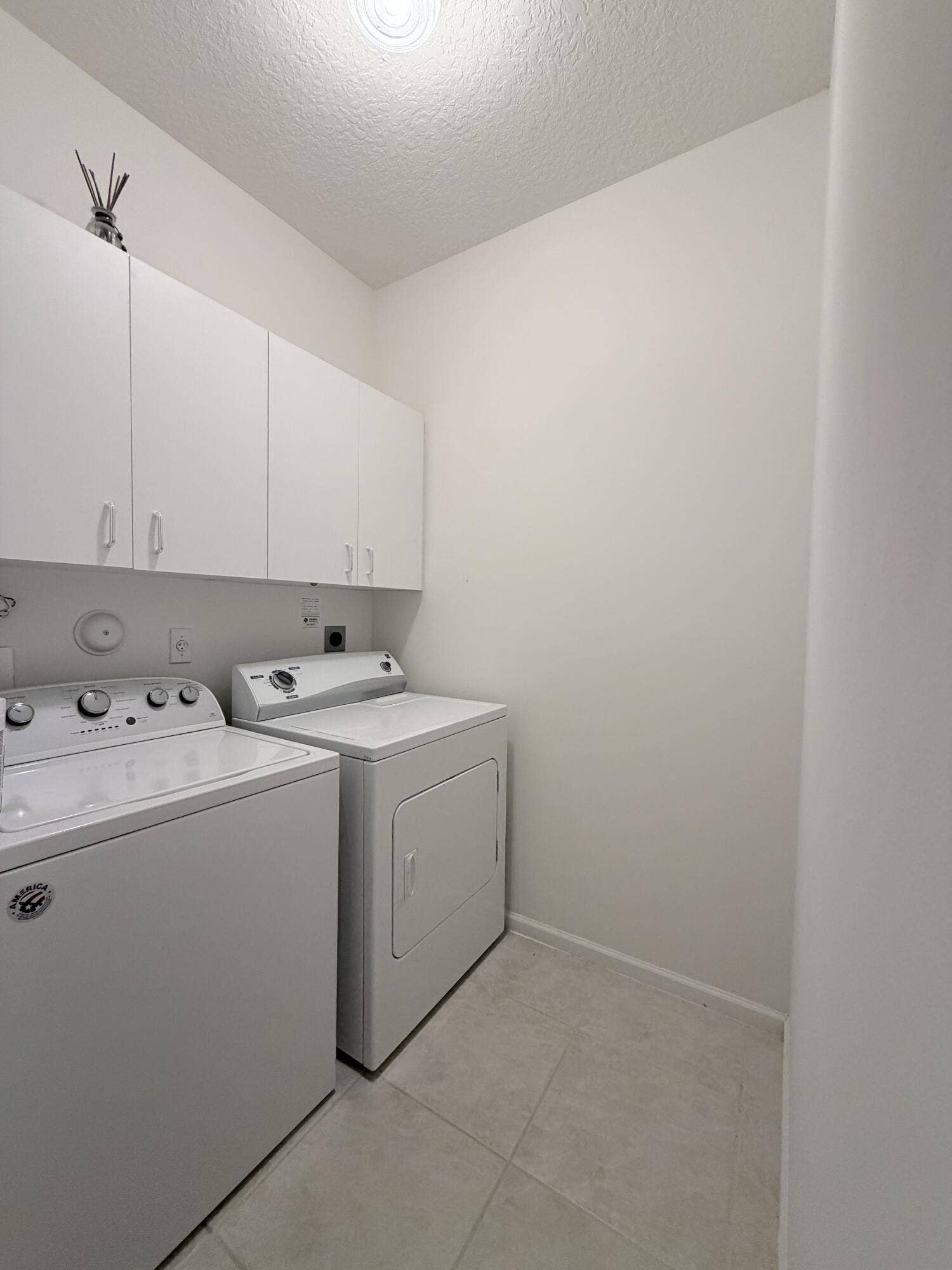 Utility space featuring white shaker-style wall-mounted cabinetry, tile flooring, and overhead lighting