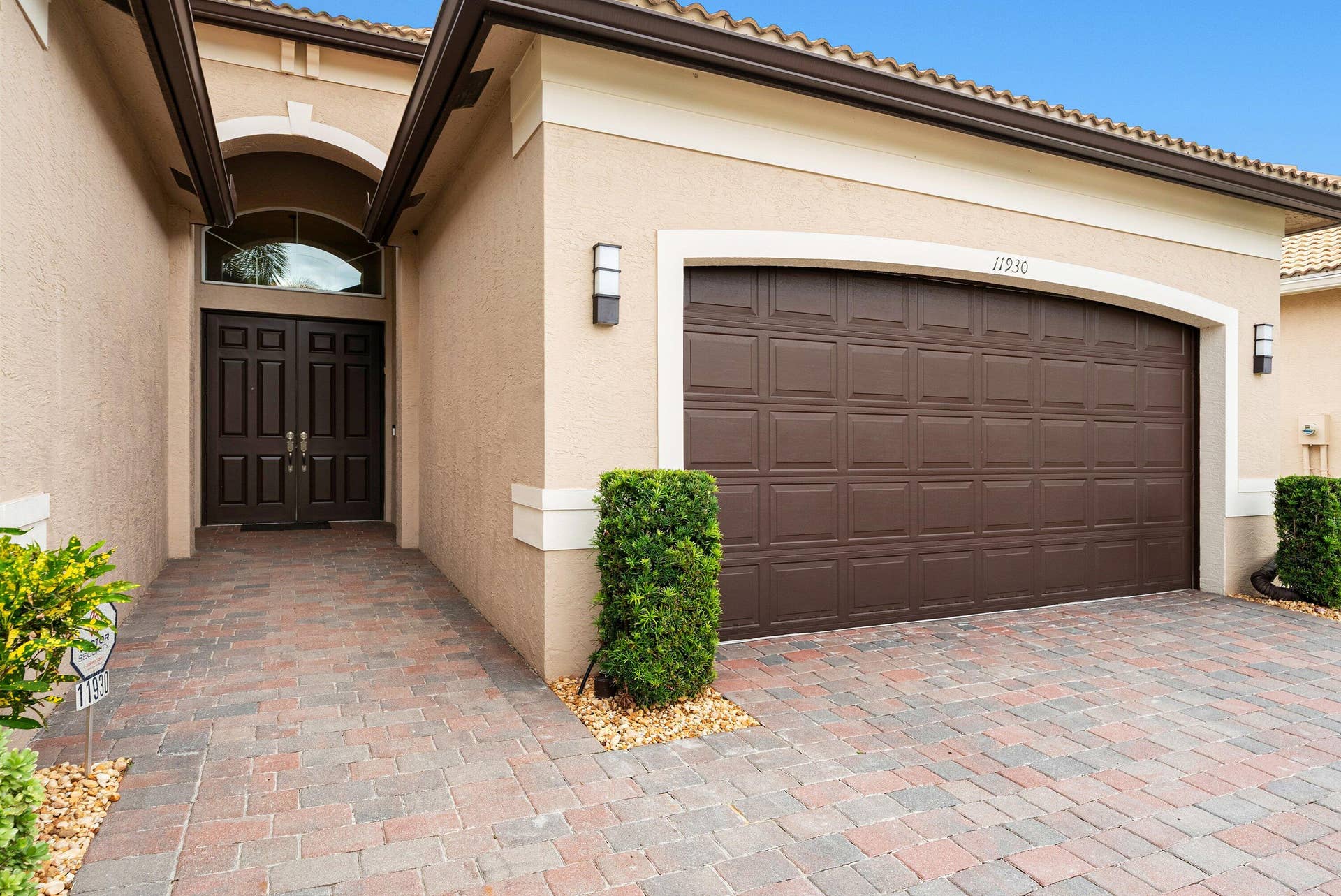 Stucco exterior featuring an arched entryway, double-panel front doors with a fanlight window, a multi-car garage with a raised-panel door, and a decorative paver driveway