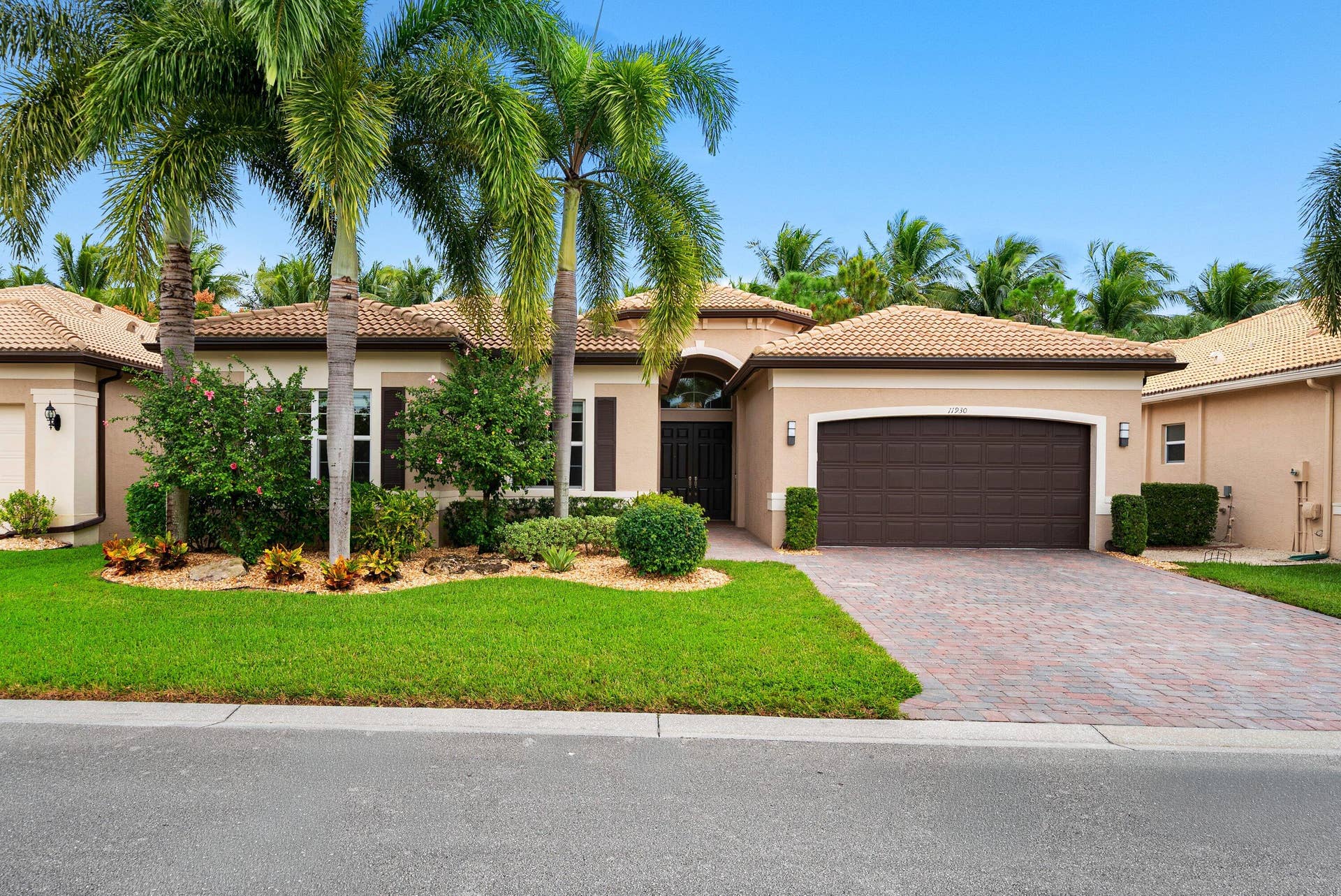 Stucco exterior featuring a multi-hipped tile roof, paver driveway, attached two-car garage, and mature palm trees