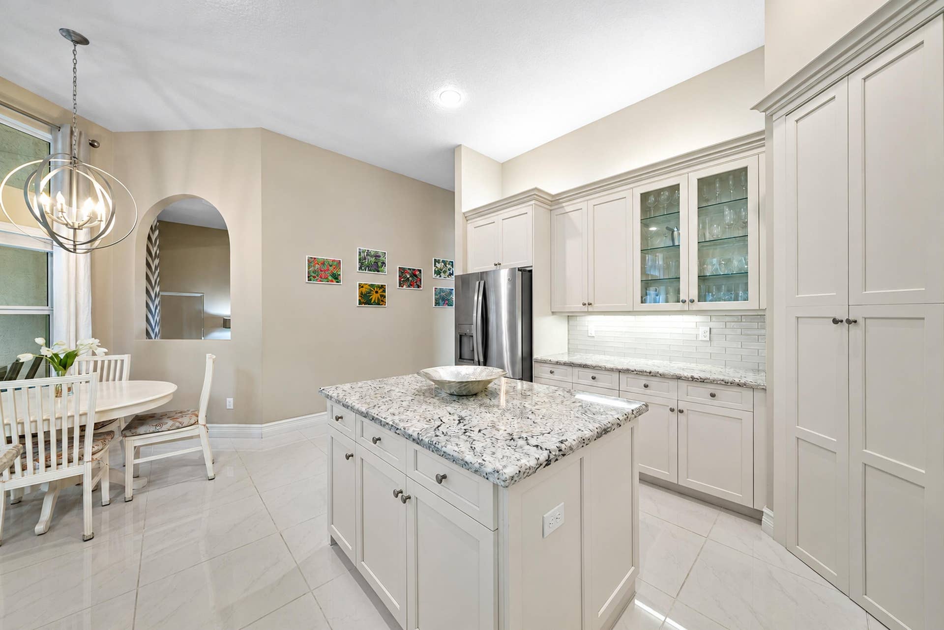 Kitchen featuring custom cabinetry with glass-front display uppers, a central island with stone countertop, stainless steel refrigerator, and tiled flooring