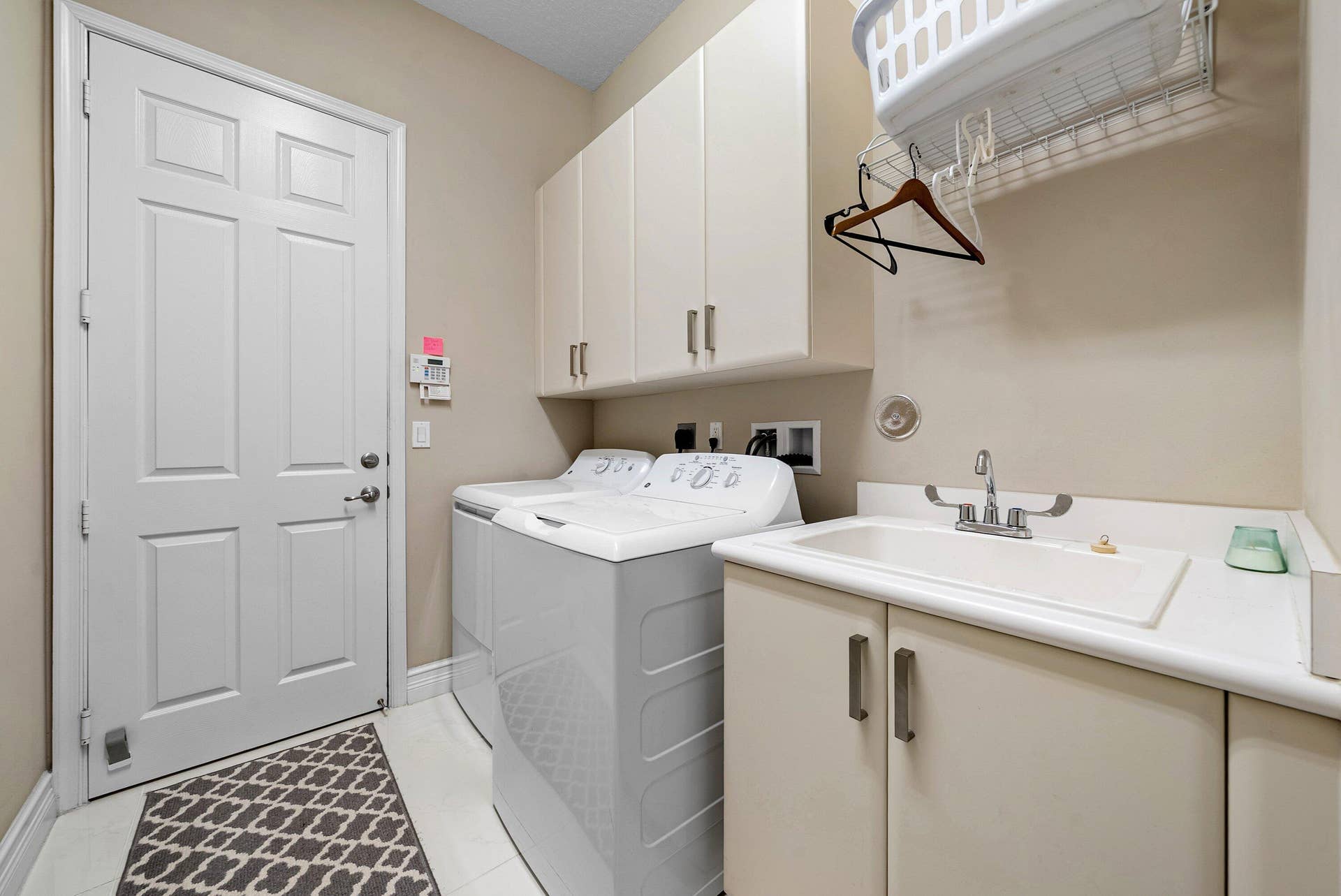 Utility room featuring upper cabinetry, a base cabinet with an integrated basin, a faucet, and white tile flooring