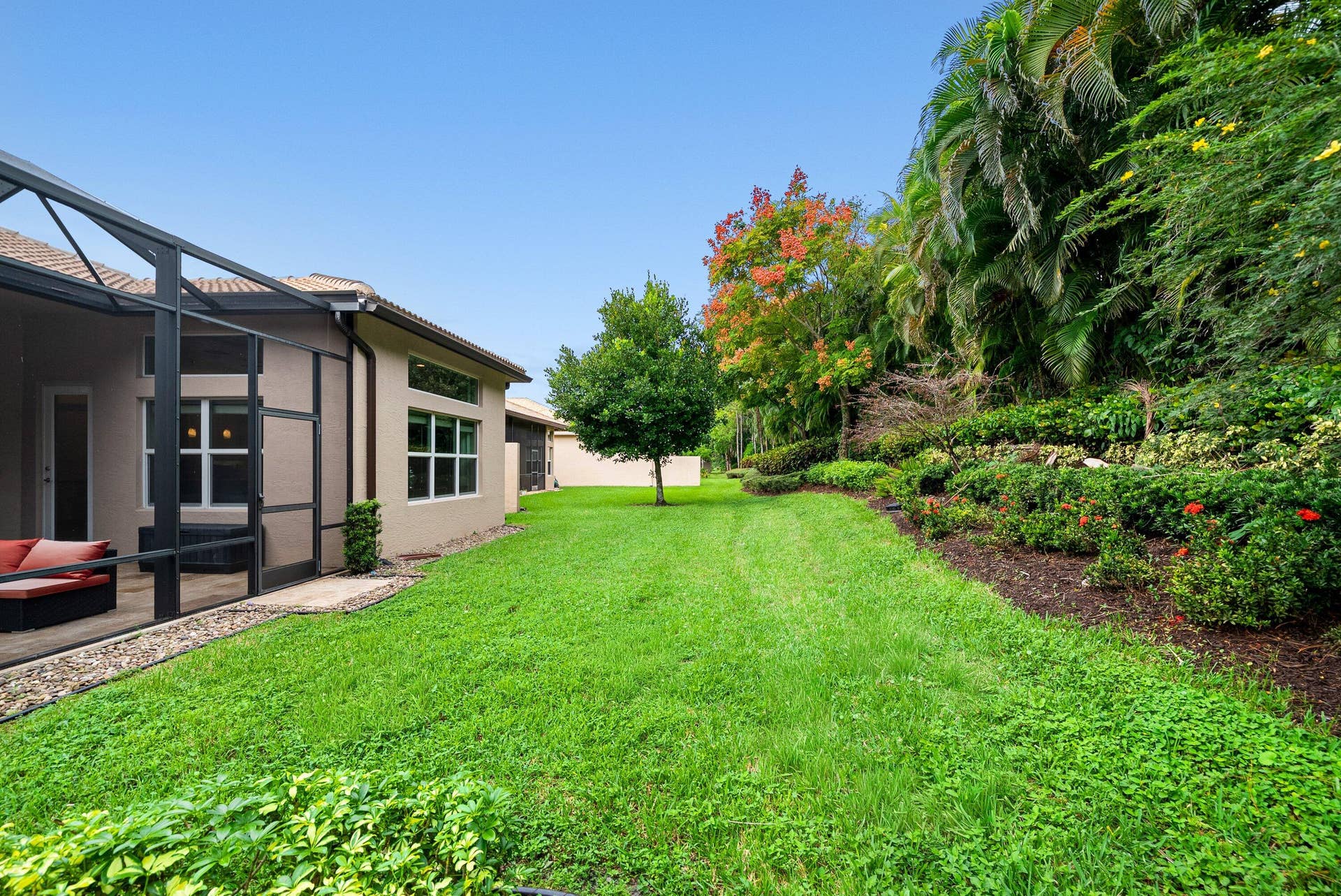 Expansive backyard featuring a screened-in patio, manicured lawn, tiered landscape beds, and mature trees