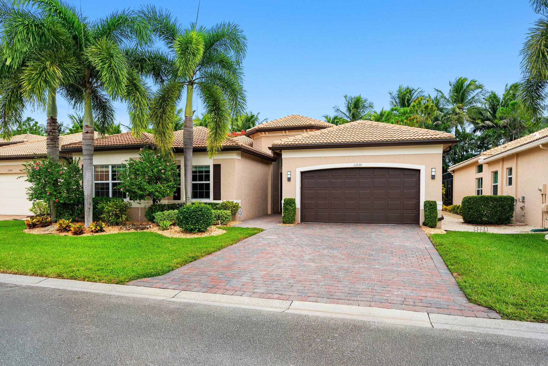 Stucco exterior residence featuring a multi-hipped tile roof, paver driveway, arched garage entry, and mature palm landscaping